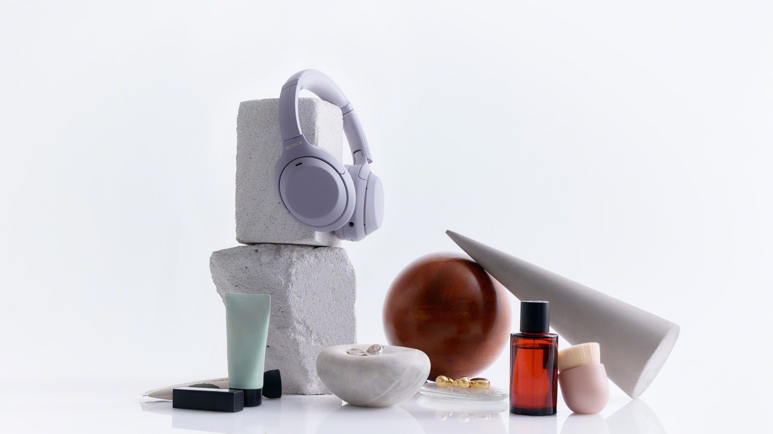Sony WH-1000XM4C on a grey plinth, with a few other items in the frame, including a perfume bottle