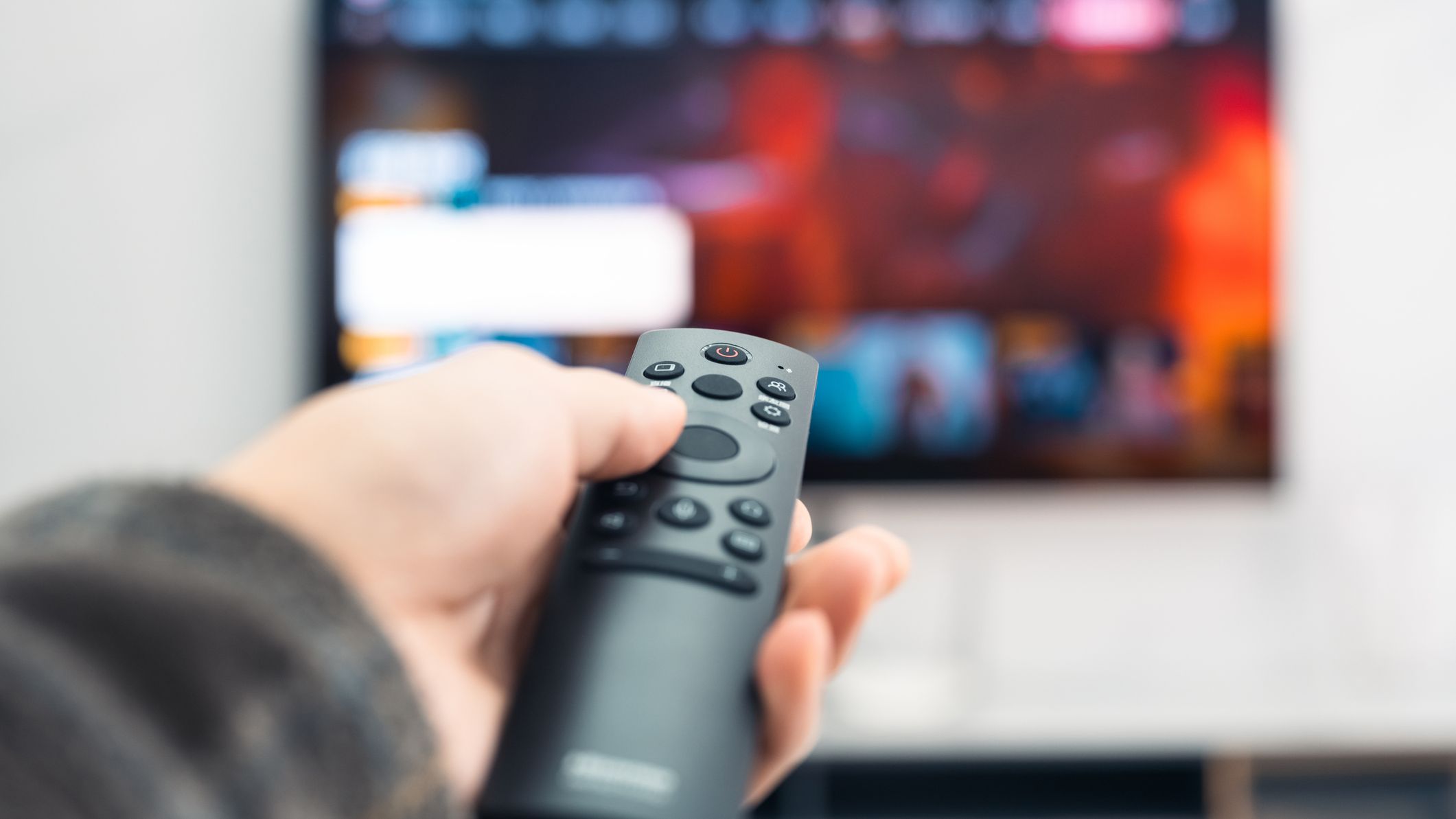 Close-up of a man holding a TV remote control in his hand.