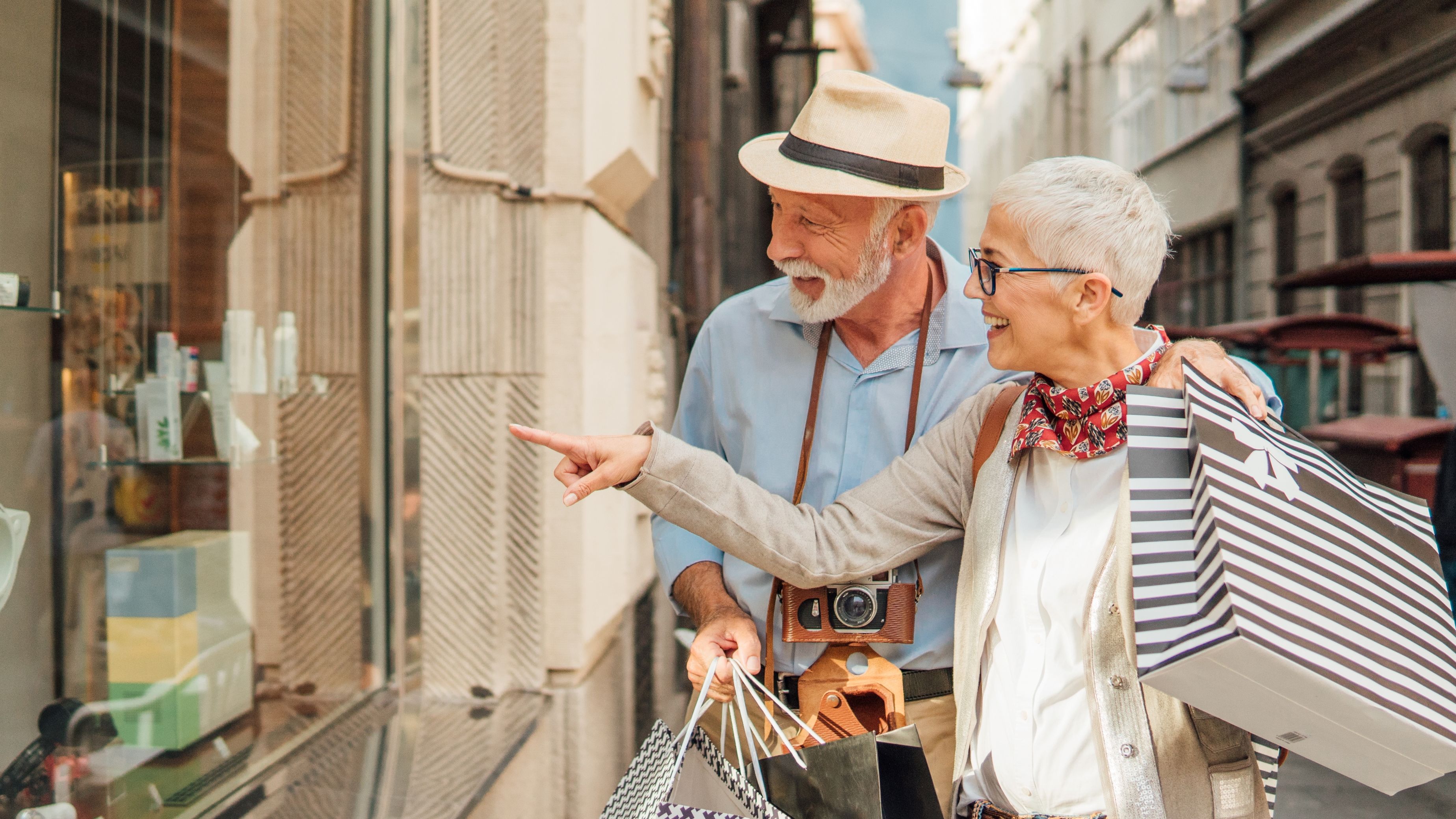 A senior couple window shopping while carrying bags.