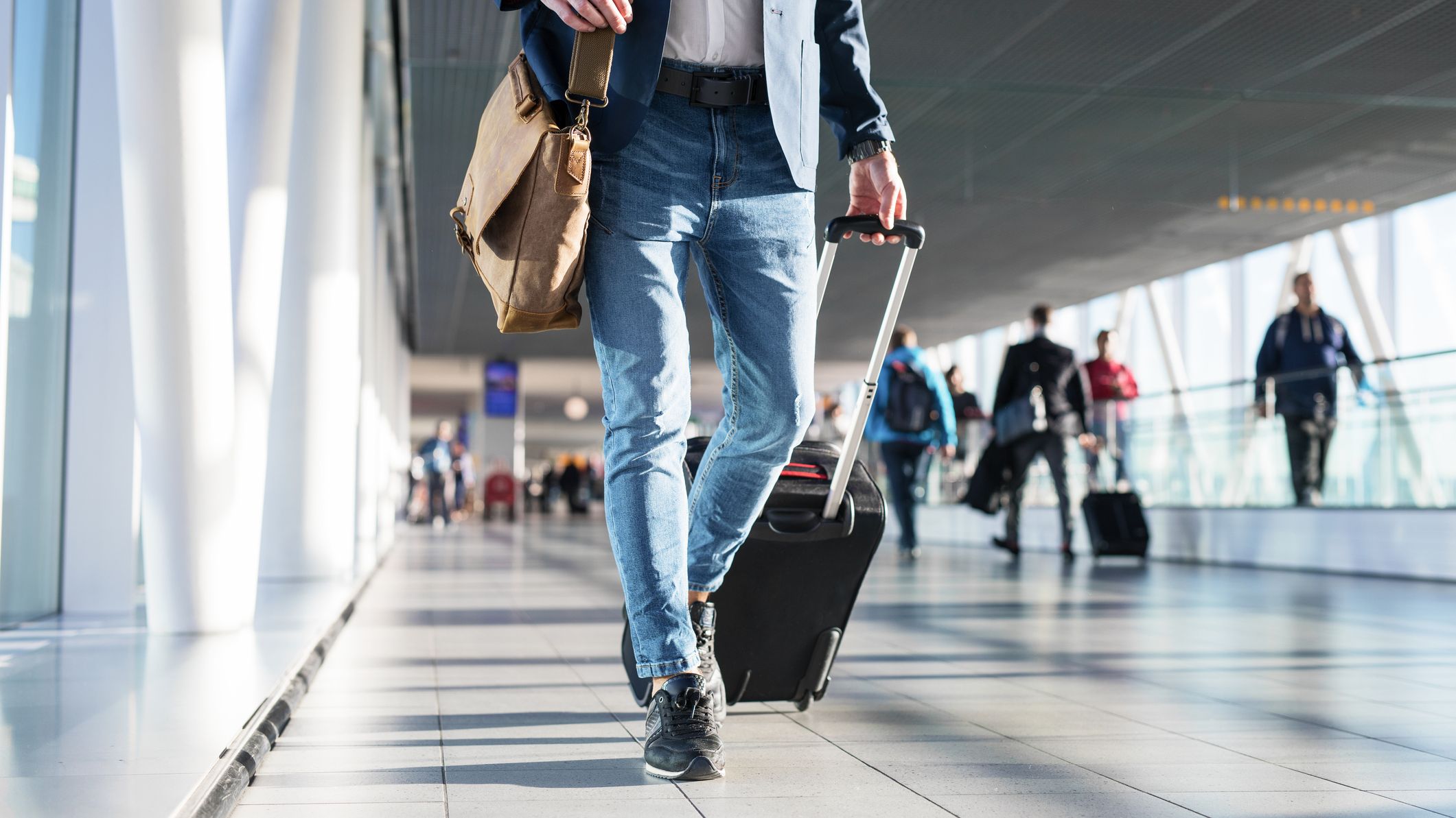 Man with shoulder bag and hand luggage walking in airport terminal