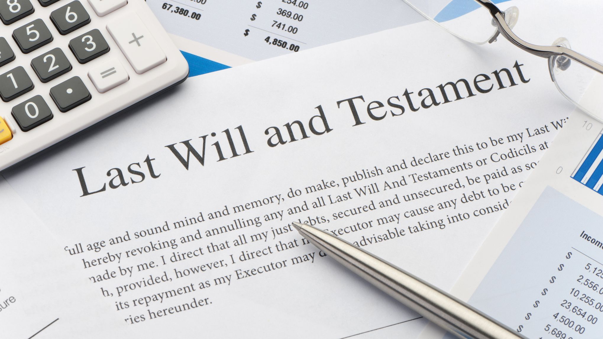 Close up of a last will and testament, calculator and other documents on a table.