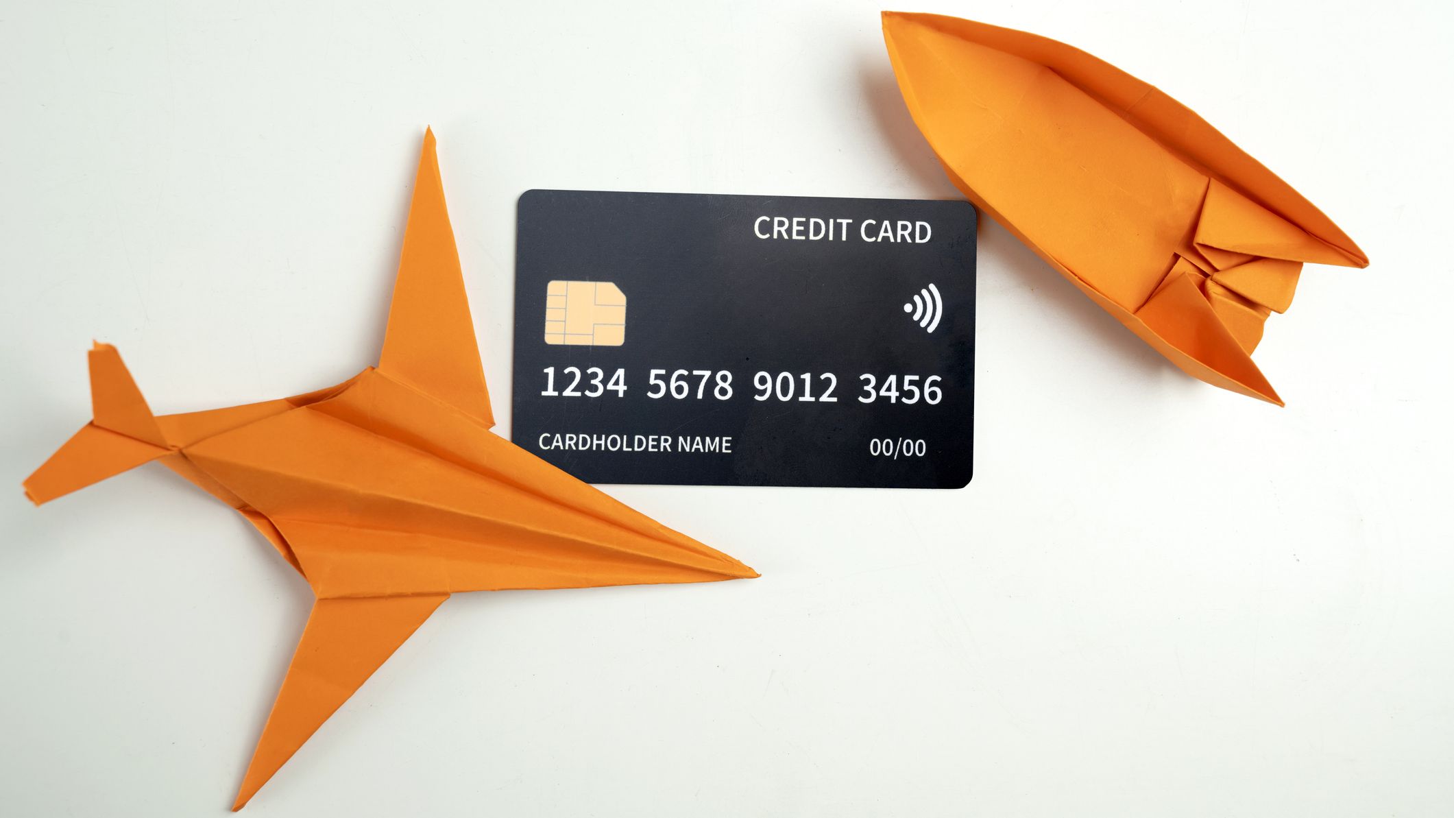 Credit card with an orange paper airplane and boat on a white background.