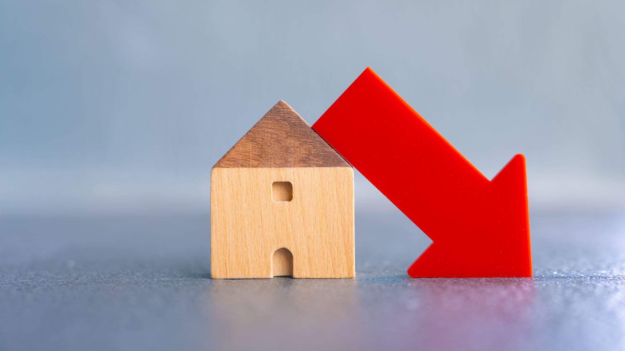 Wooden house model with red down arrow.