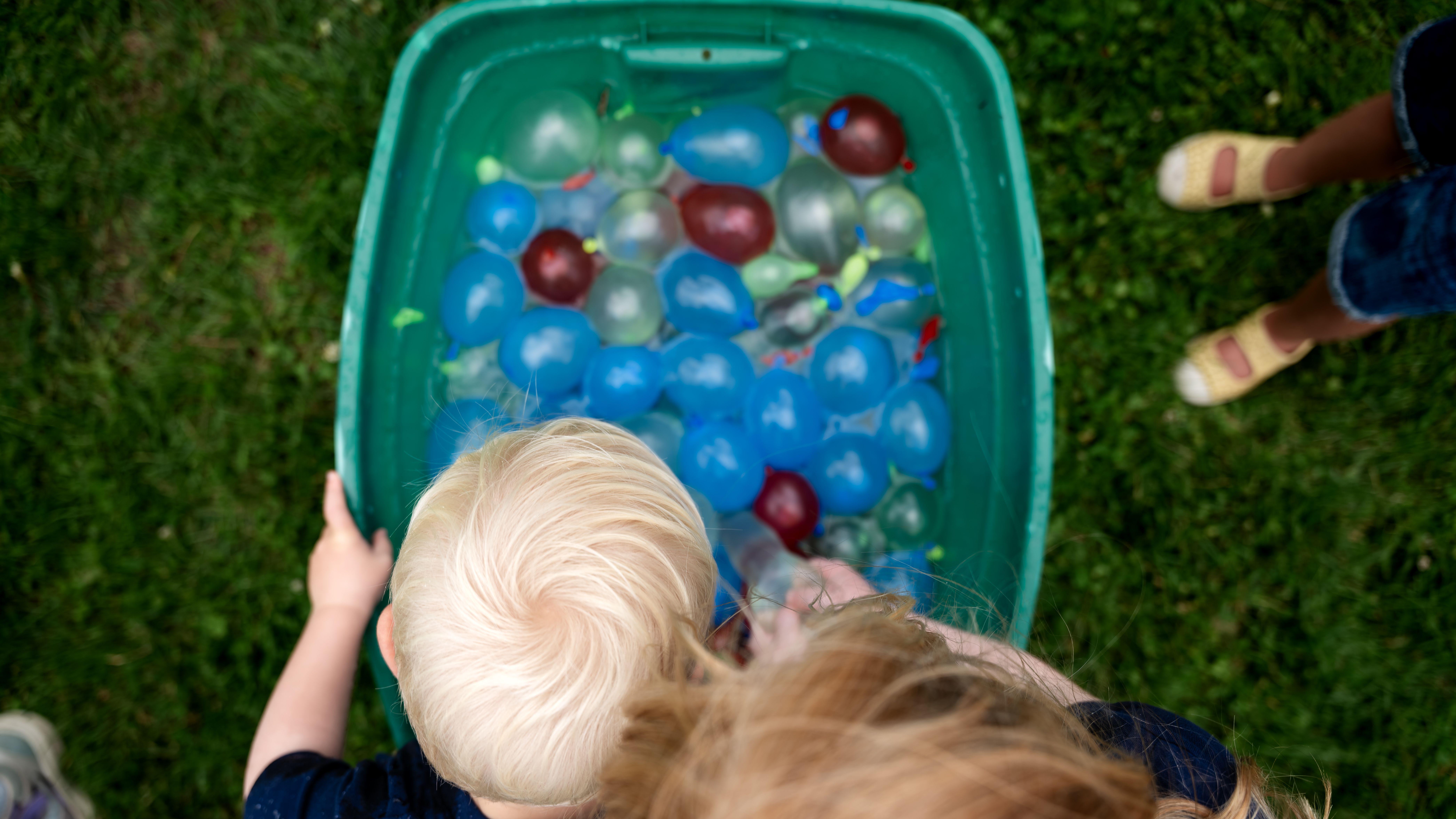 A group of children take water balloons from a bin at a family reunion.