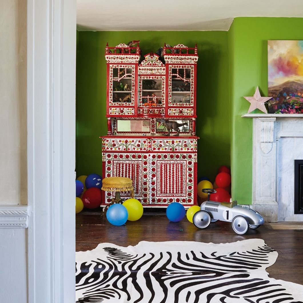 Children's playroom with bright green painted walls, antique decorated dresser, fake cowhide rug and vintage toys