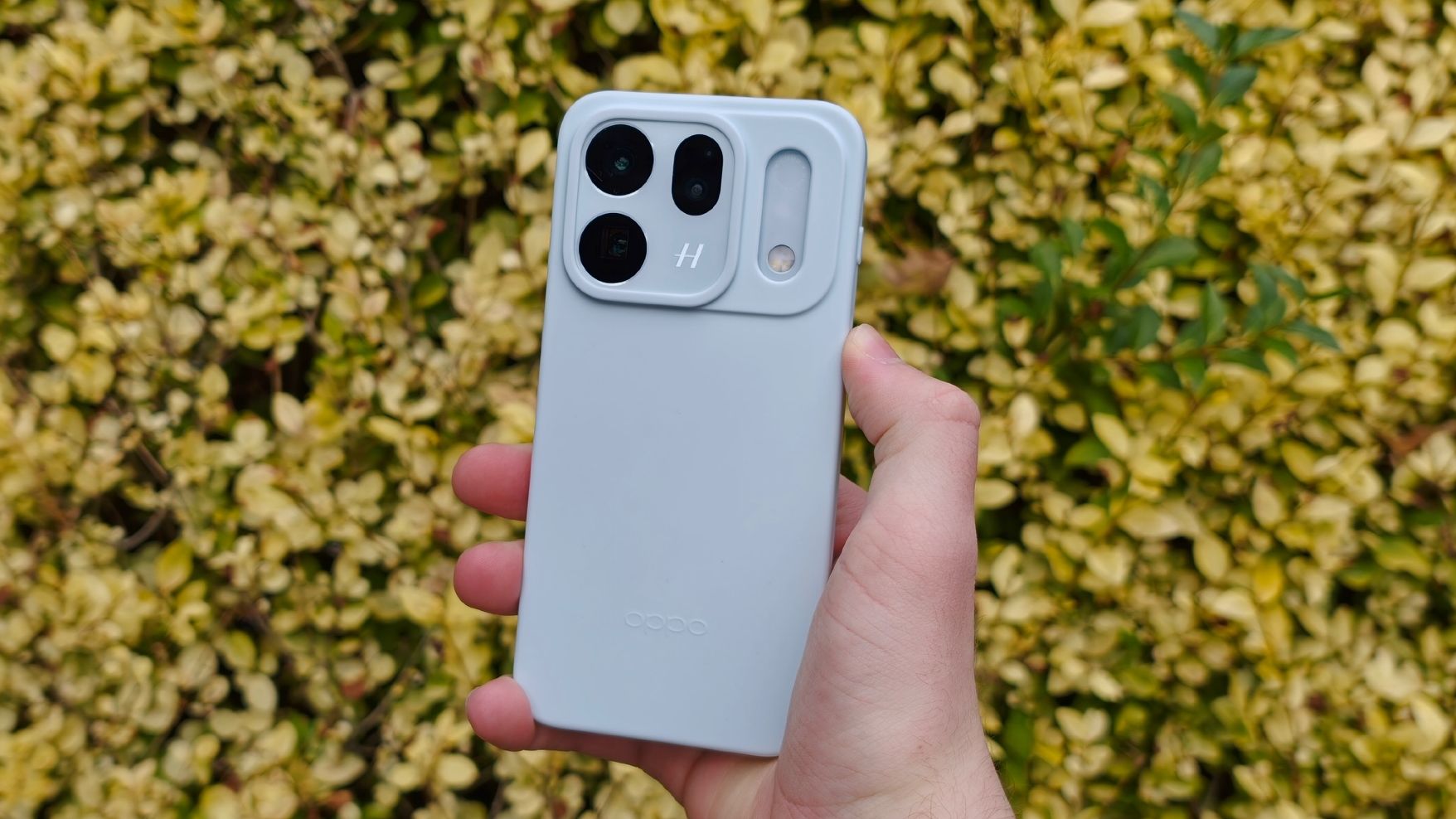 The Oppo Find X10 in a silicone case against a wall of yellow leaves