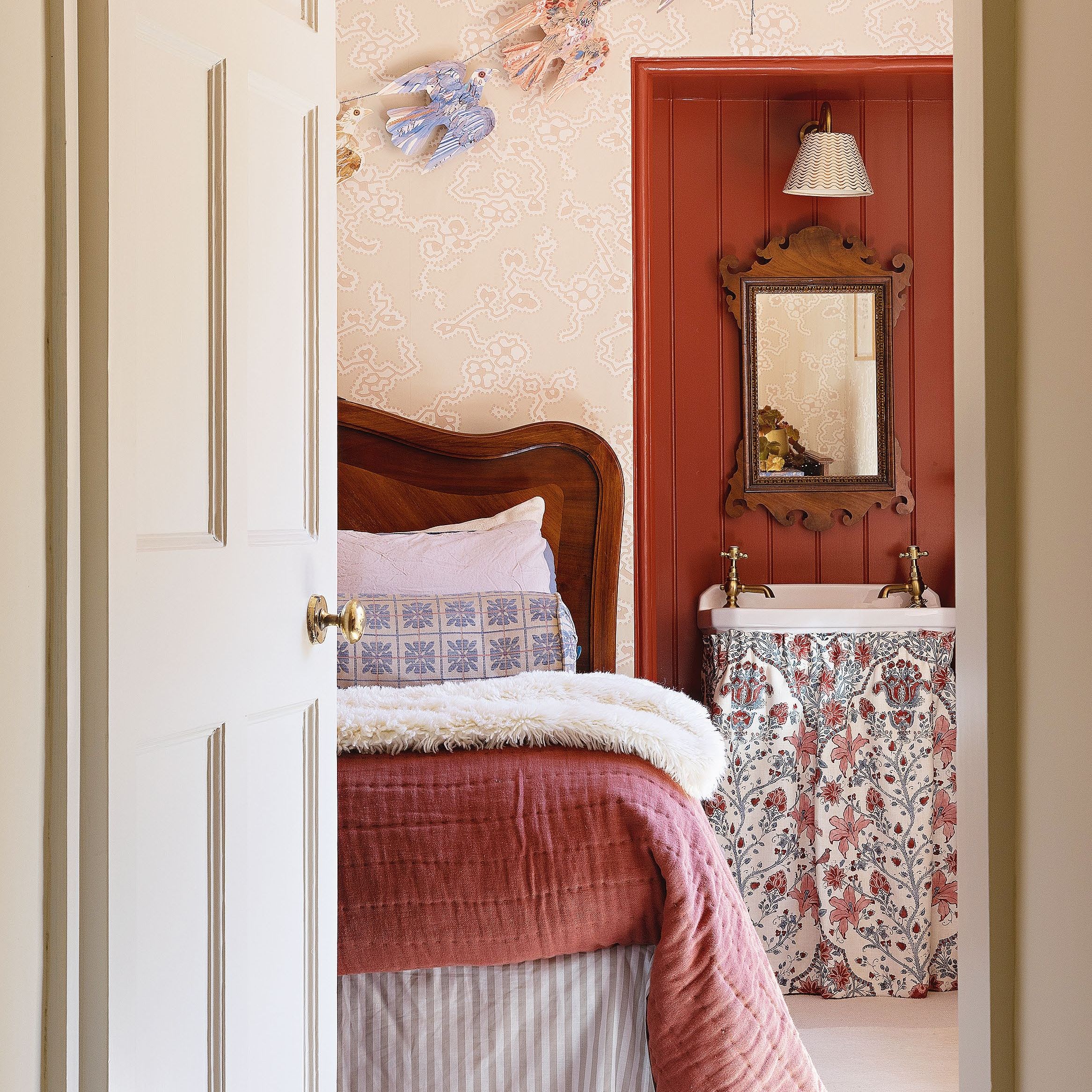 Bedroom with pink patterned wallpaper and dark red panelled alcove with basin and mirror