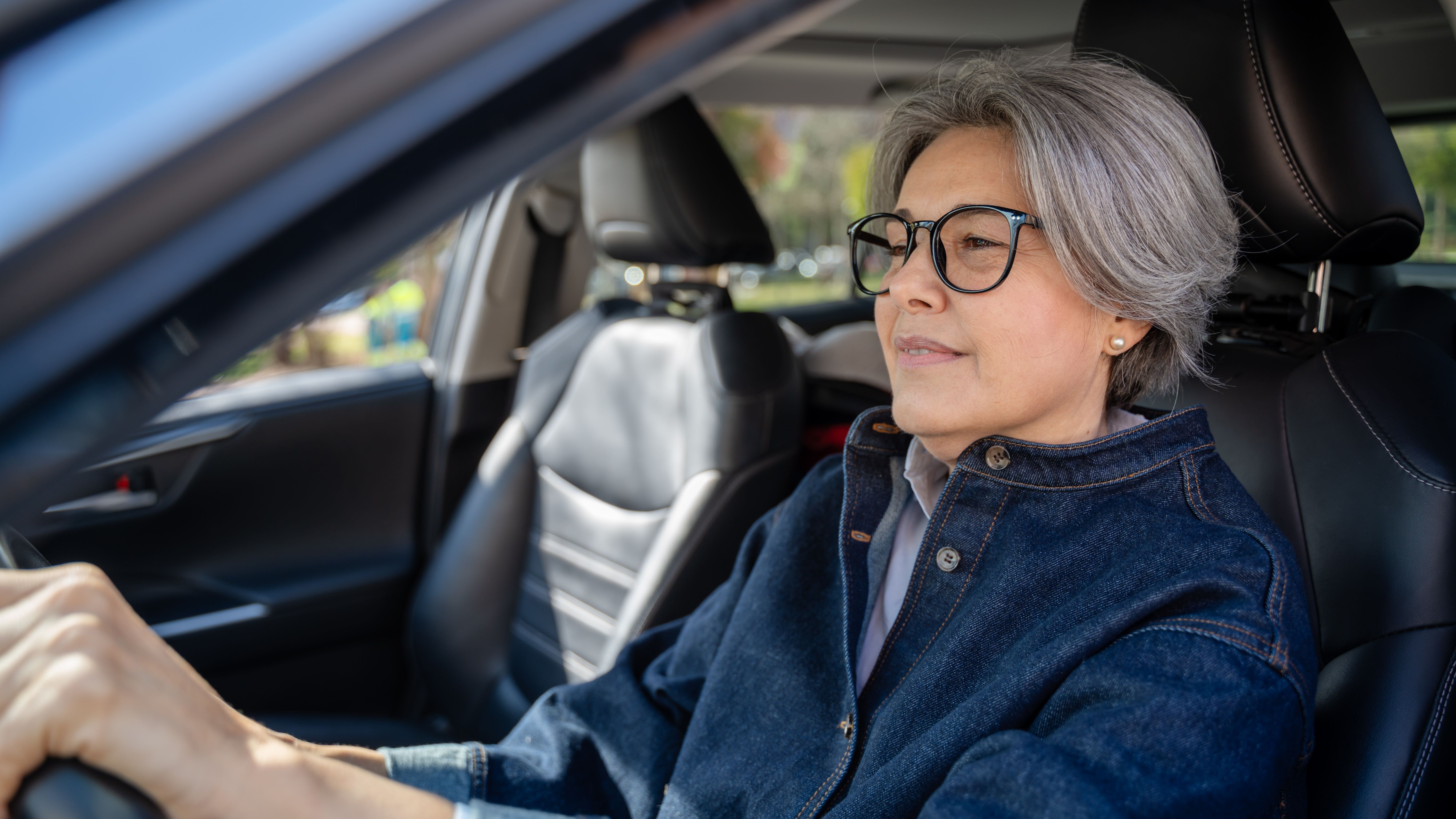 A senior woman with glasses is driving a car.