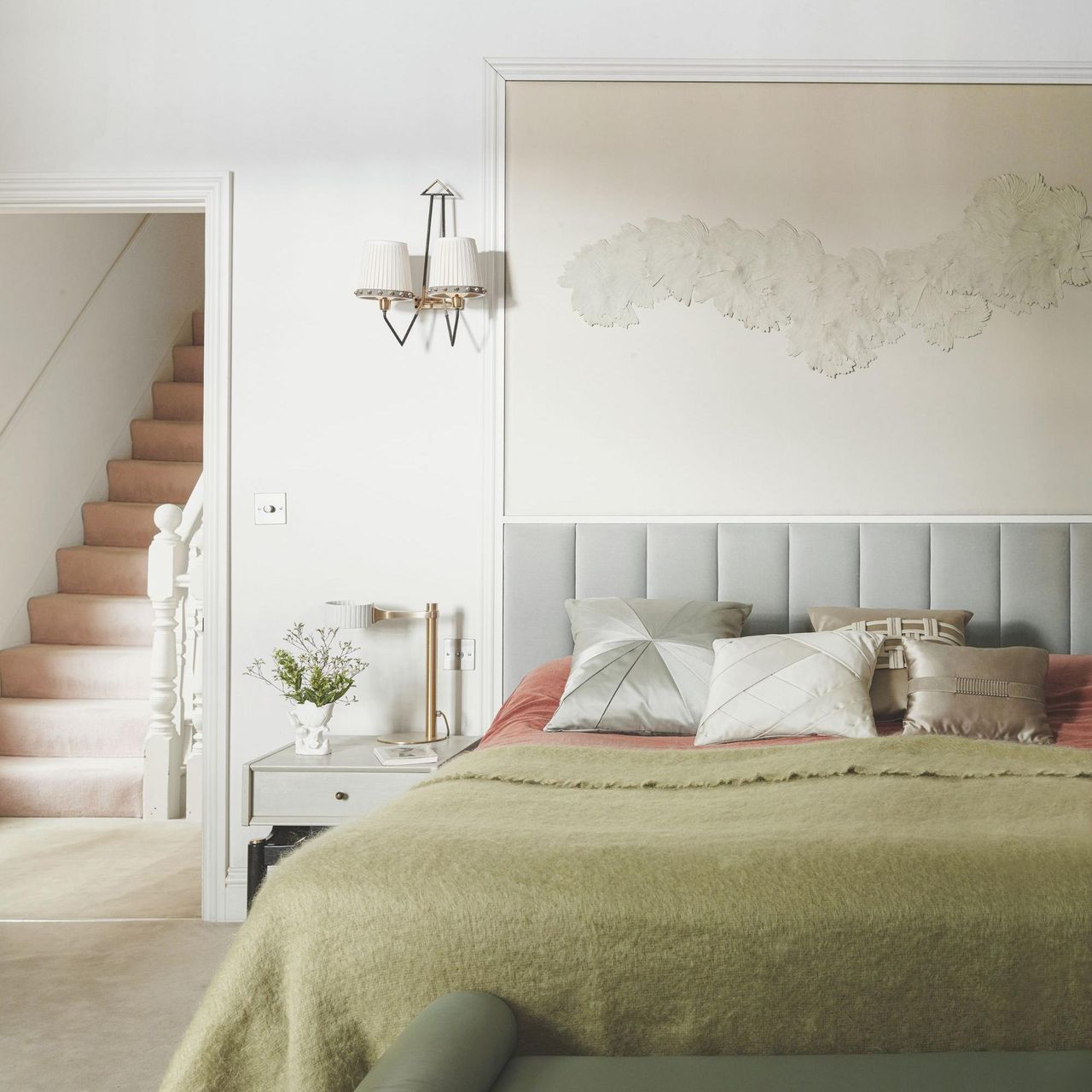 Green and gray bedding on a gray bed frame against cream walls; to the left, a cream nightstand.