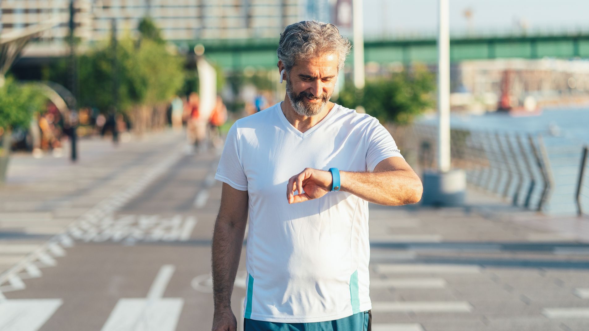 Man walking in city next to body of water looking at a blue sports watch
