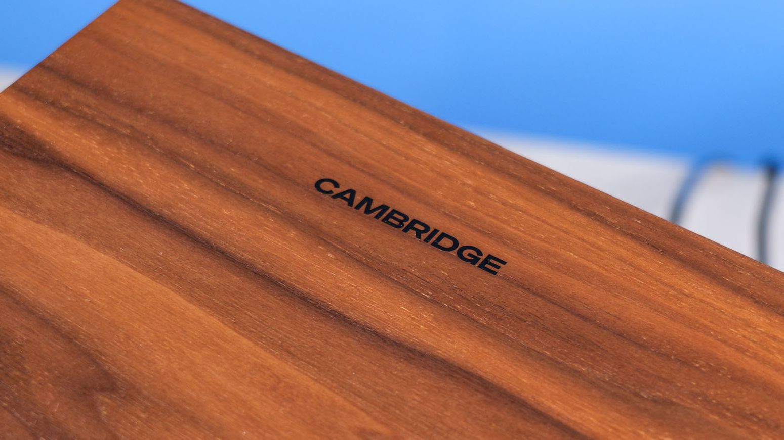 The Cambridge Audio L/R X speakers top surface, in walnut color, positioned on a stone surface with a blue background