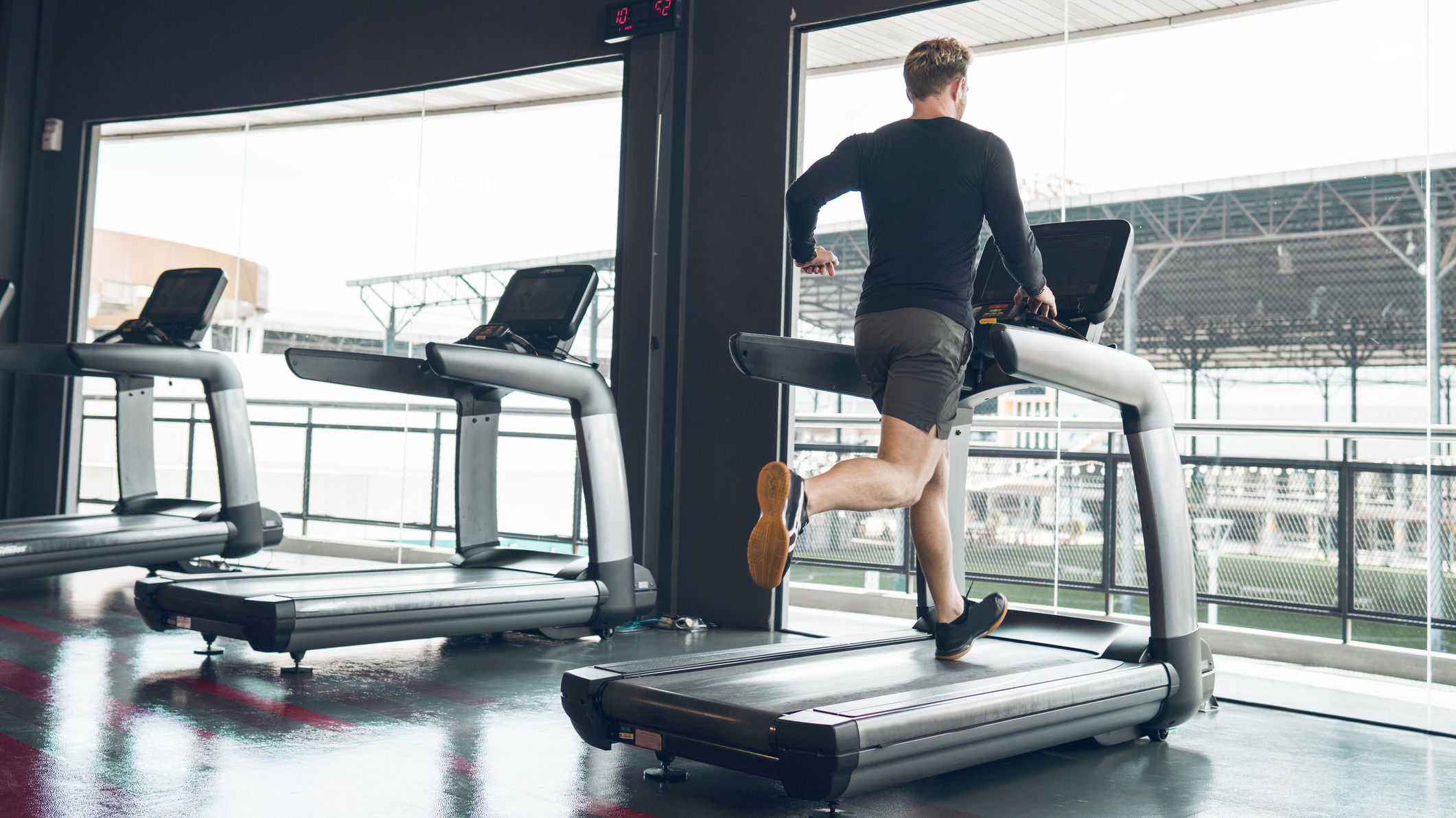 Man running on treadmill in gym seen from behind