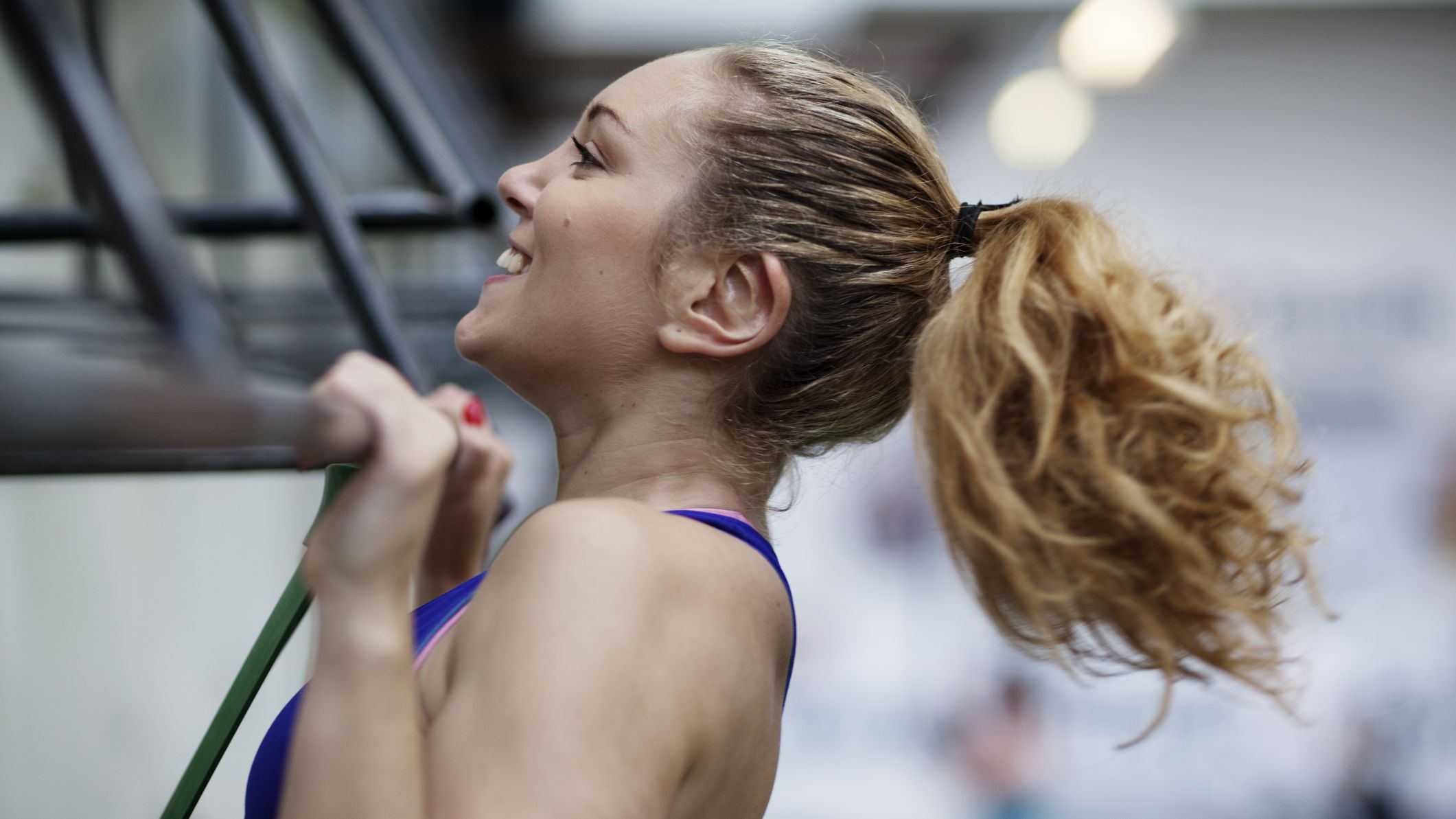 Smiling woman performing a pull-up in a gym, with her chin above the bar