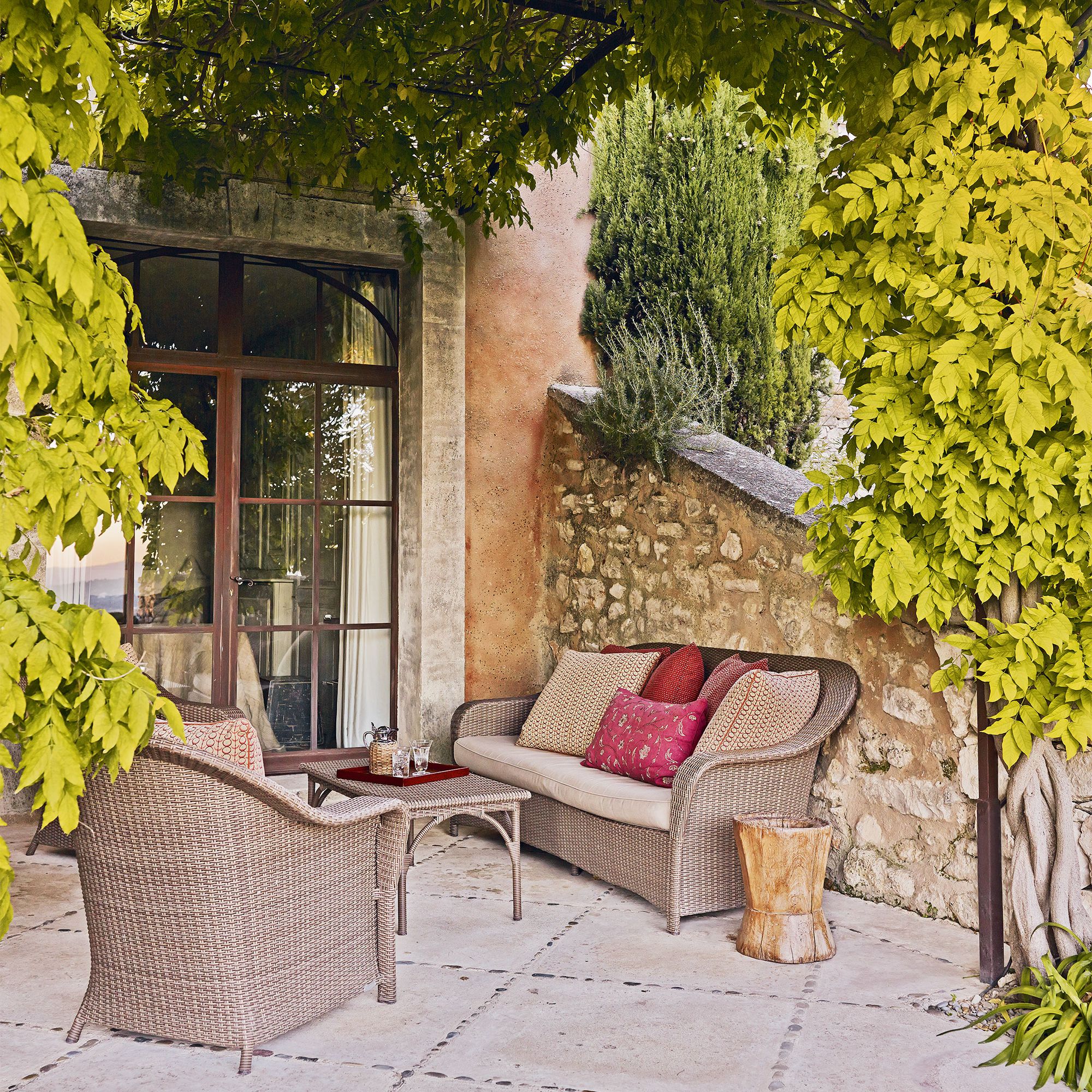 A dry stone terrace in Provence with vines and a wicker sofa illustrating Mediterranean garden ideas.