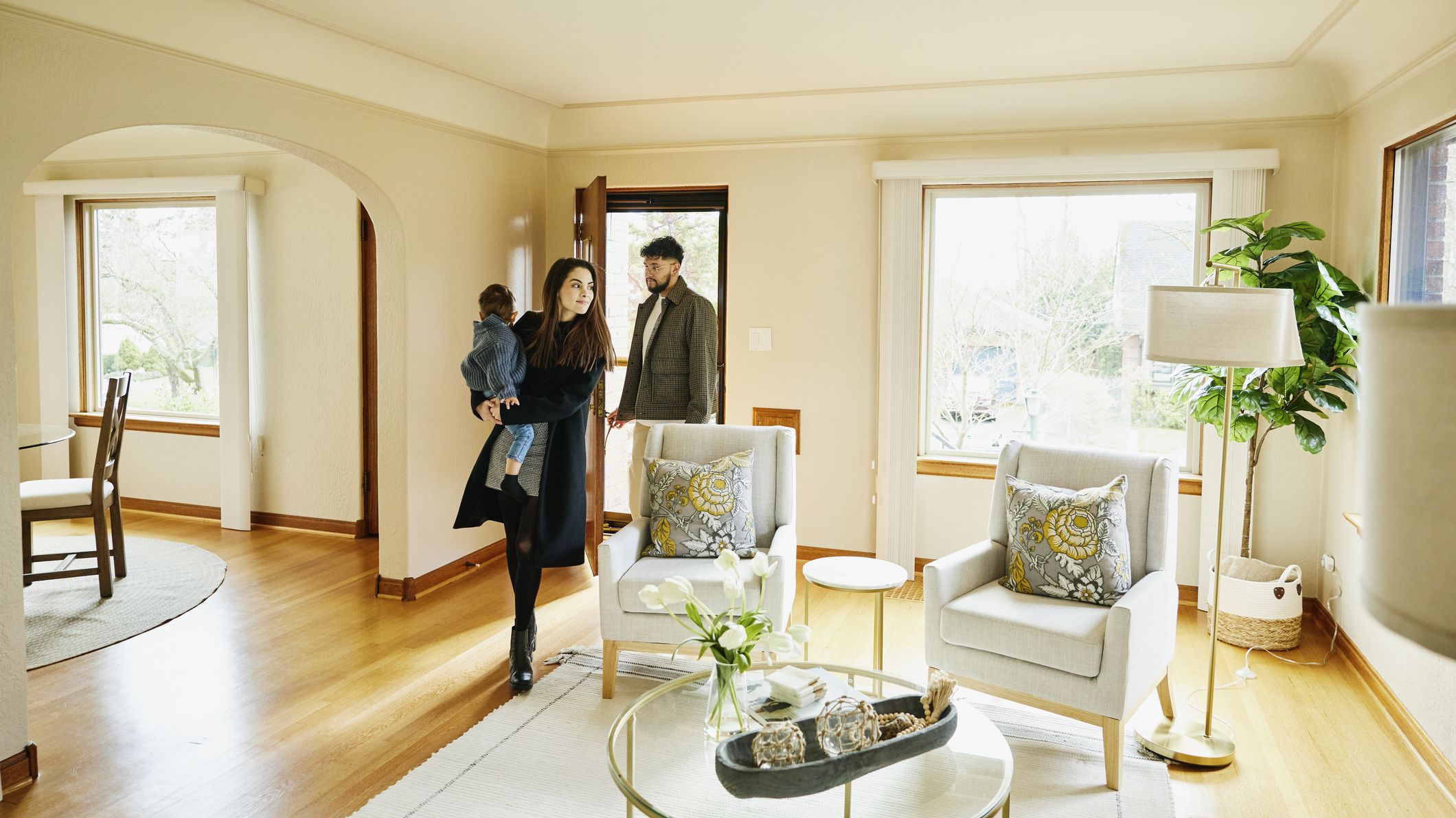 Wide shot of family with toddler walking though front door into living room of home for sale during open house