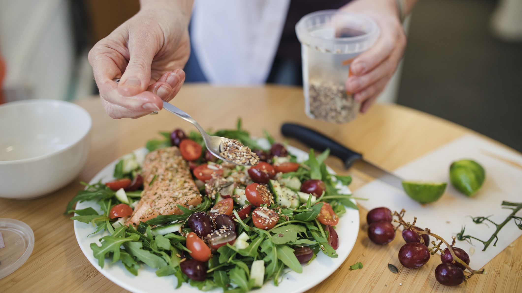 Person spooning mixed seeds onto salmon on a bed of salad