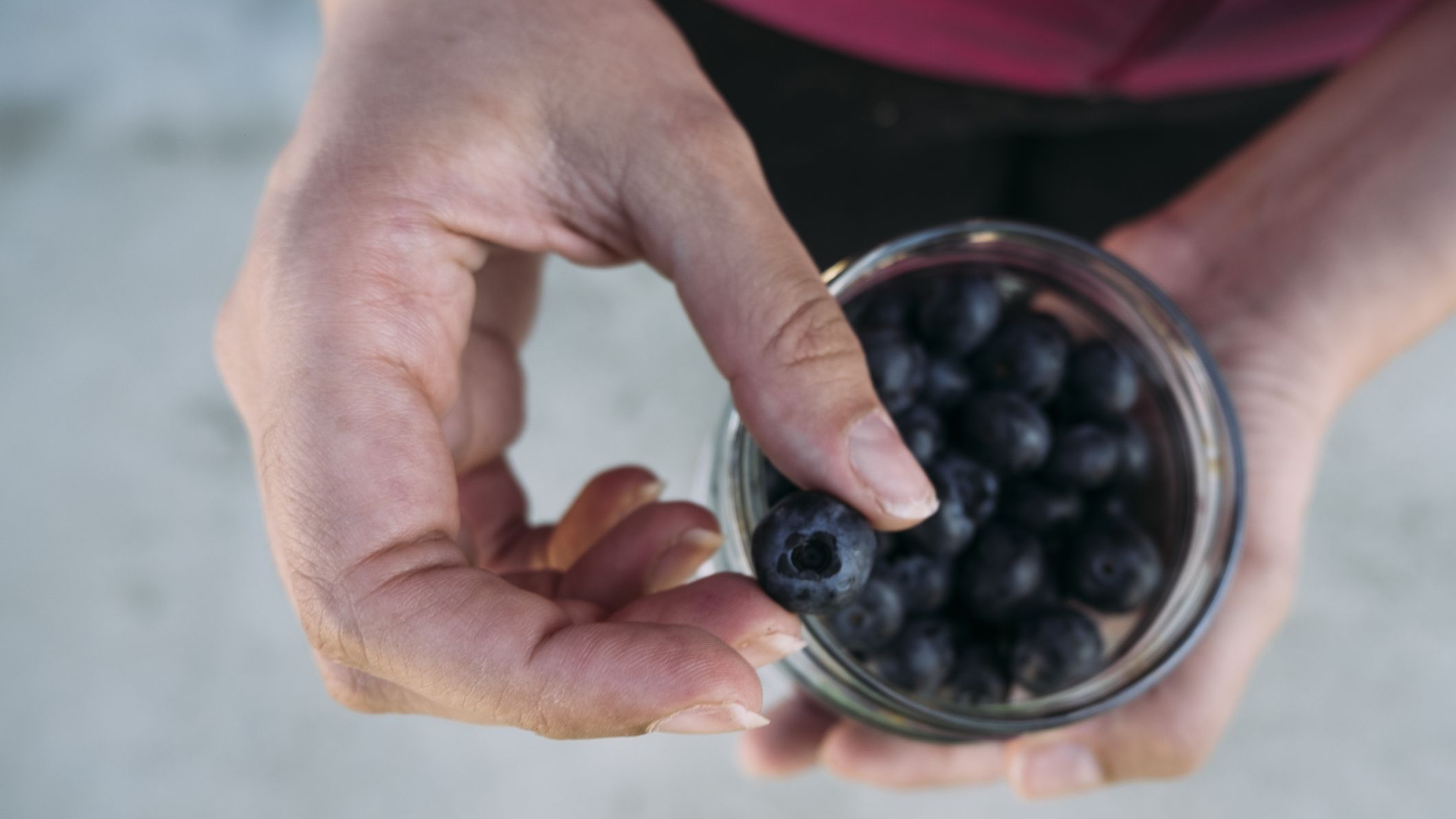 Woman holding a jar of blueberries and picking one to eat