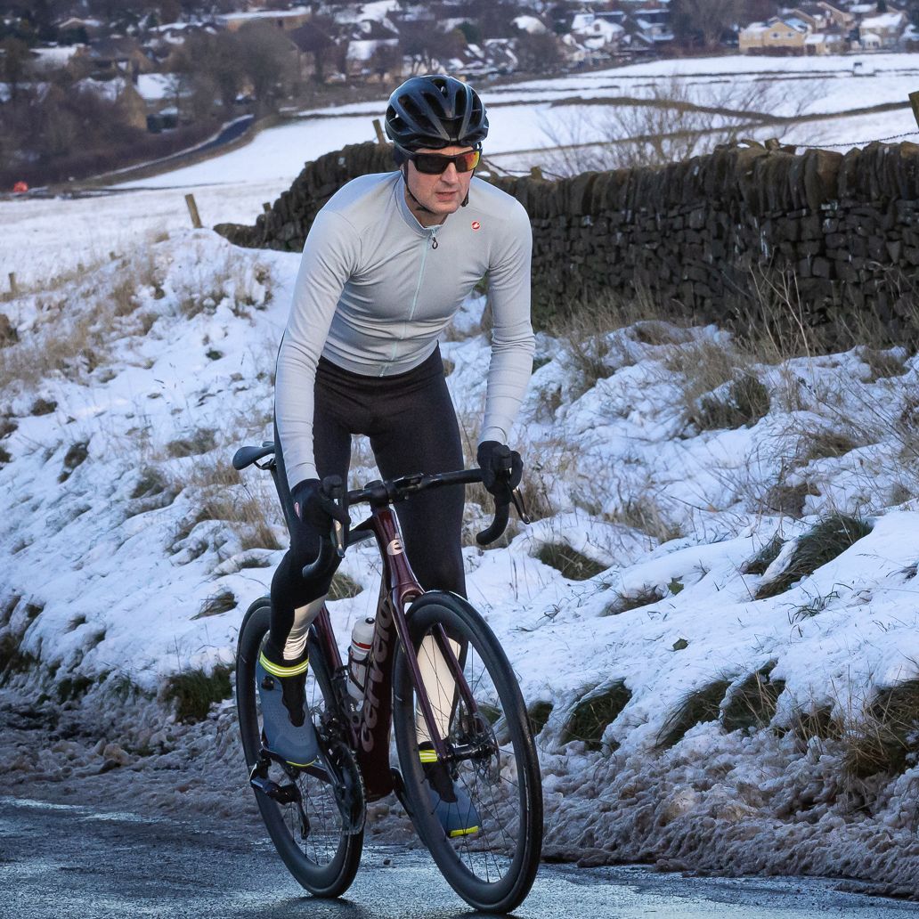 Male cyclist riding up a snowy lane wearing a pale blue jersey