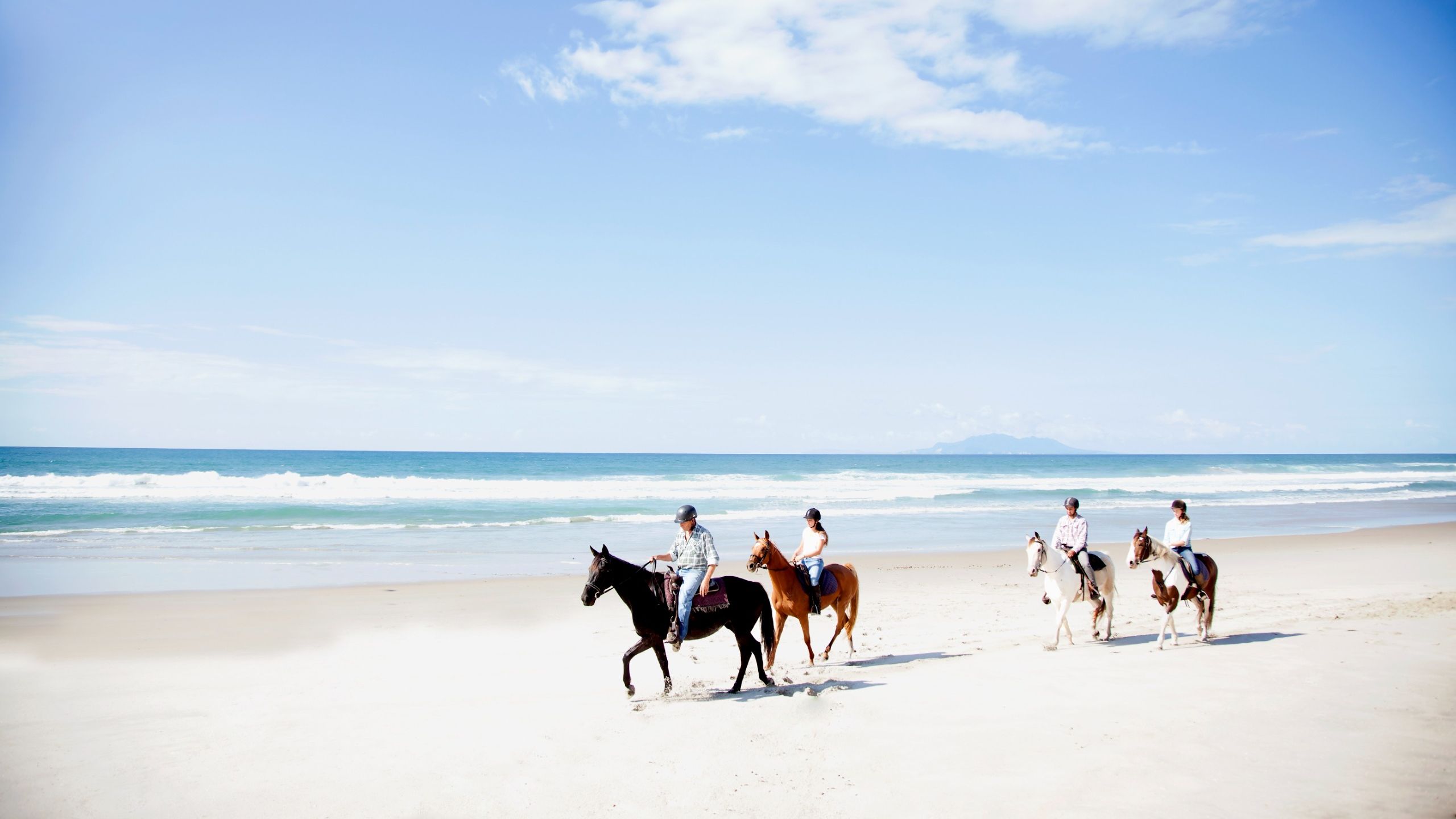 landscape view four riders hacking on a white sand beach