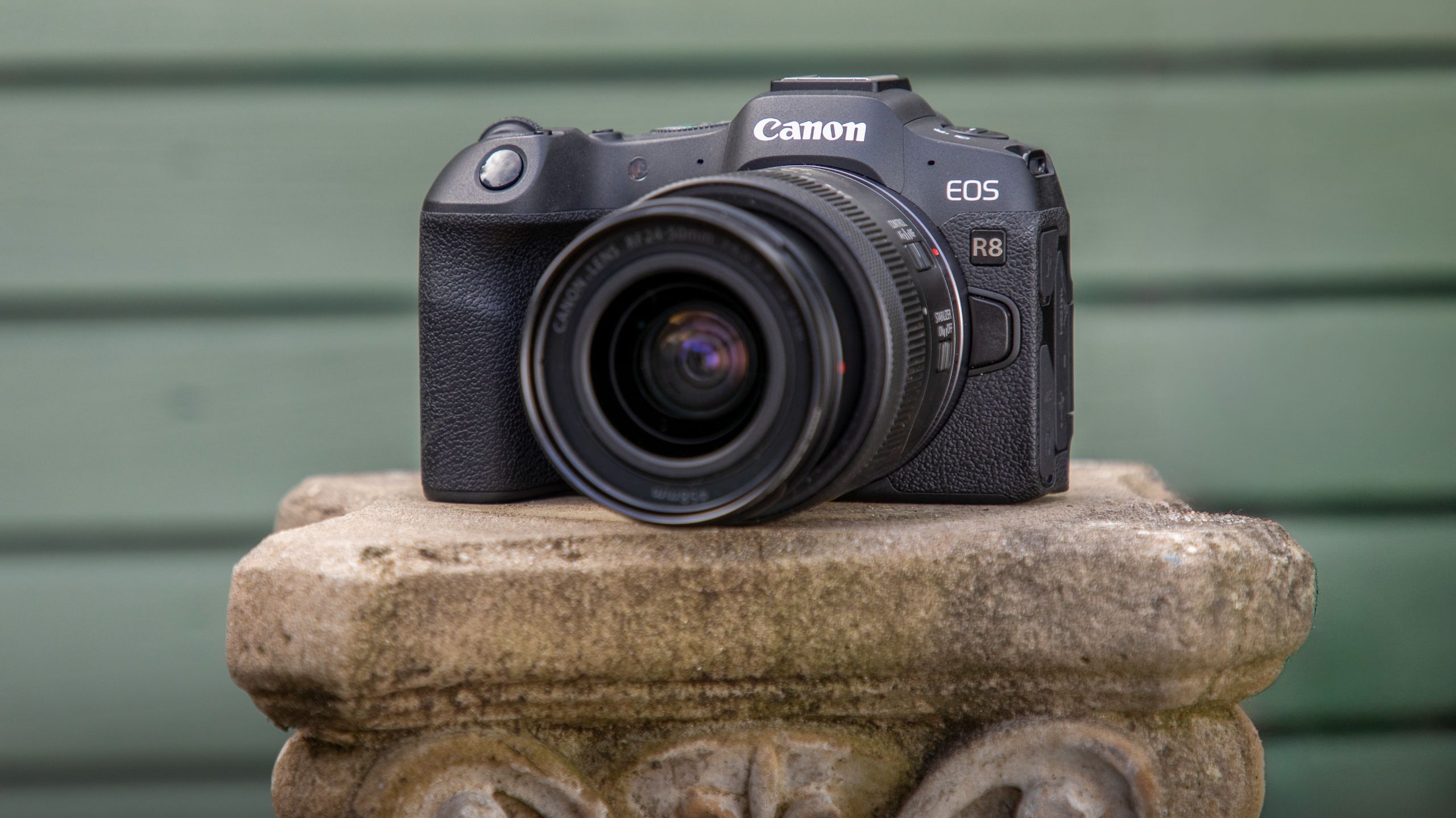 EOS R8 camera and lens in front of green woodwork