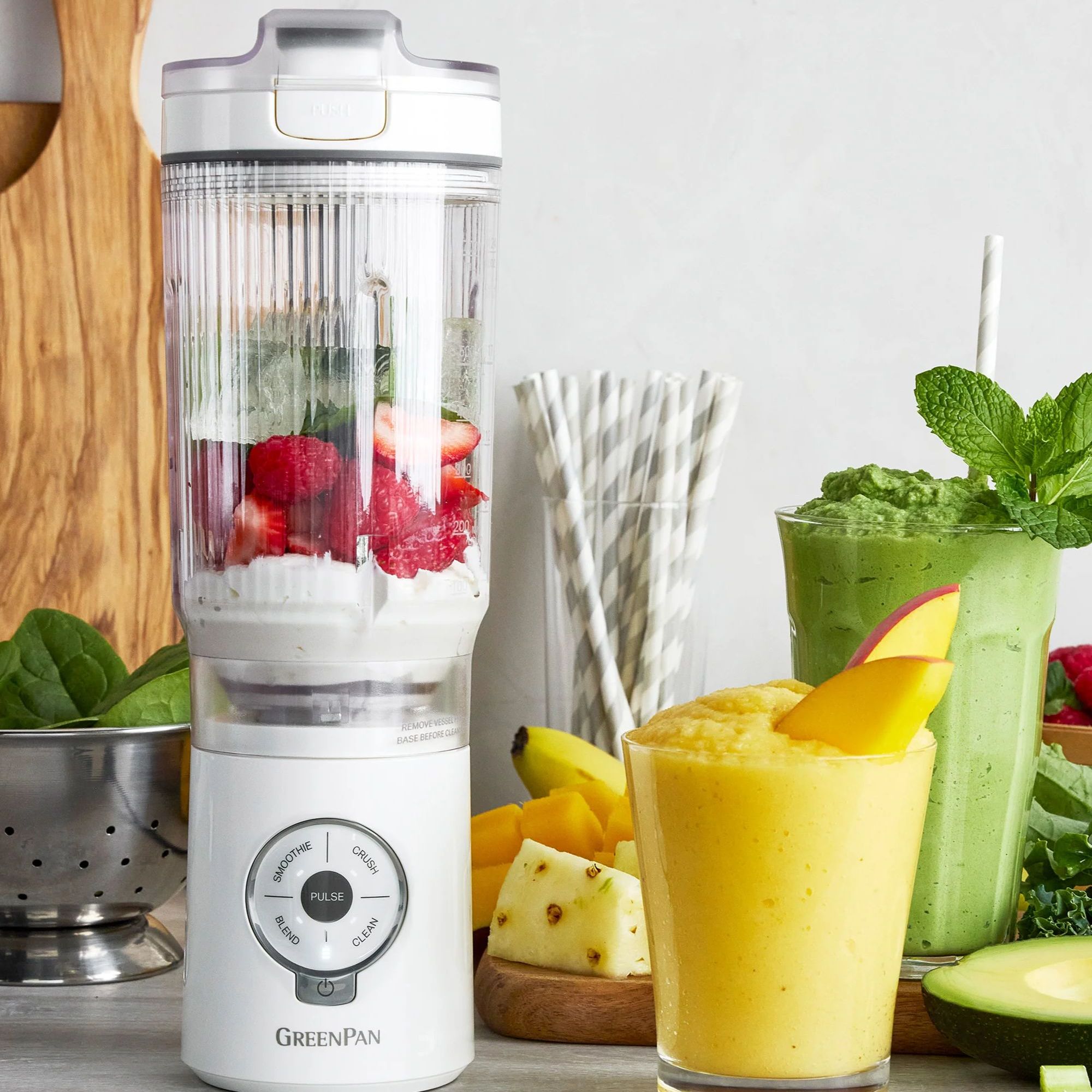 A white GreenPan spin &amp; go blender with fresh fruit inside beside a glass of a yellow smoothie.