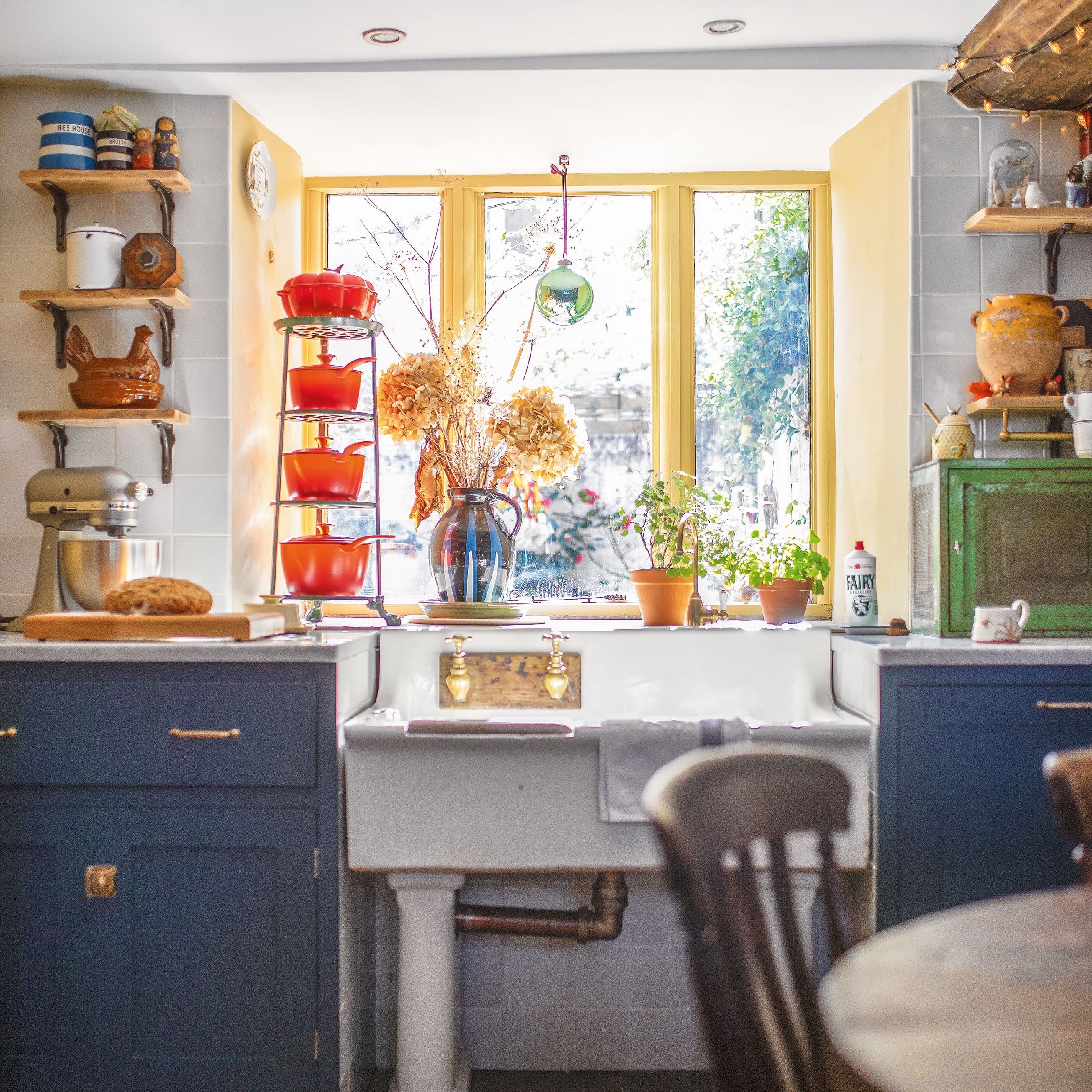 Country cottage kitchen with blue cabinets and yellow-painted windowframes above pillar sink