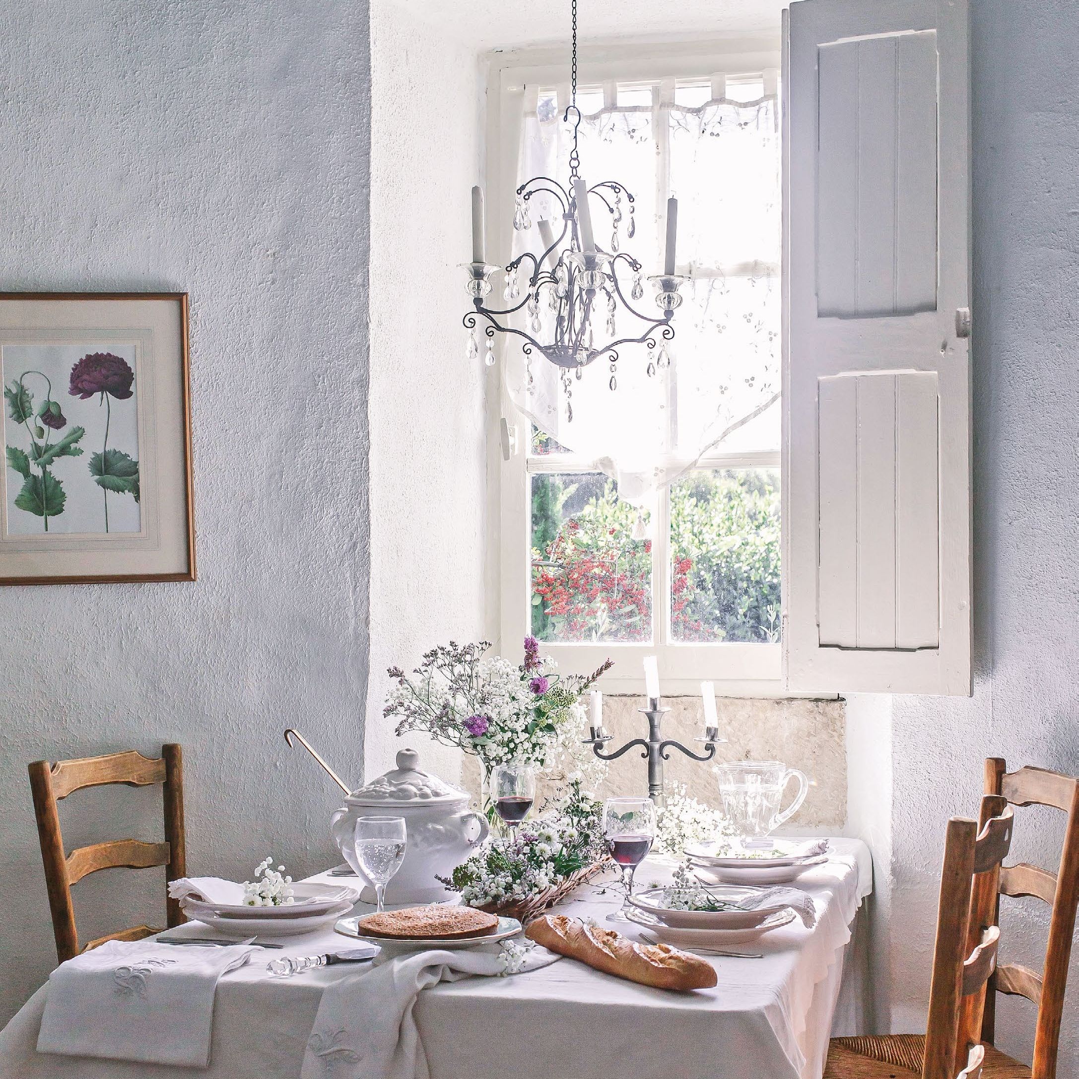 Dining table dressed with white tablecloth in front of shuttered window in a French stone tower with whitewashed walls