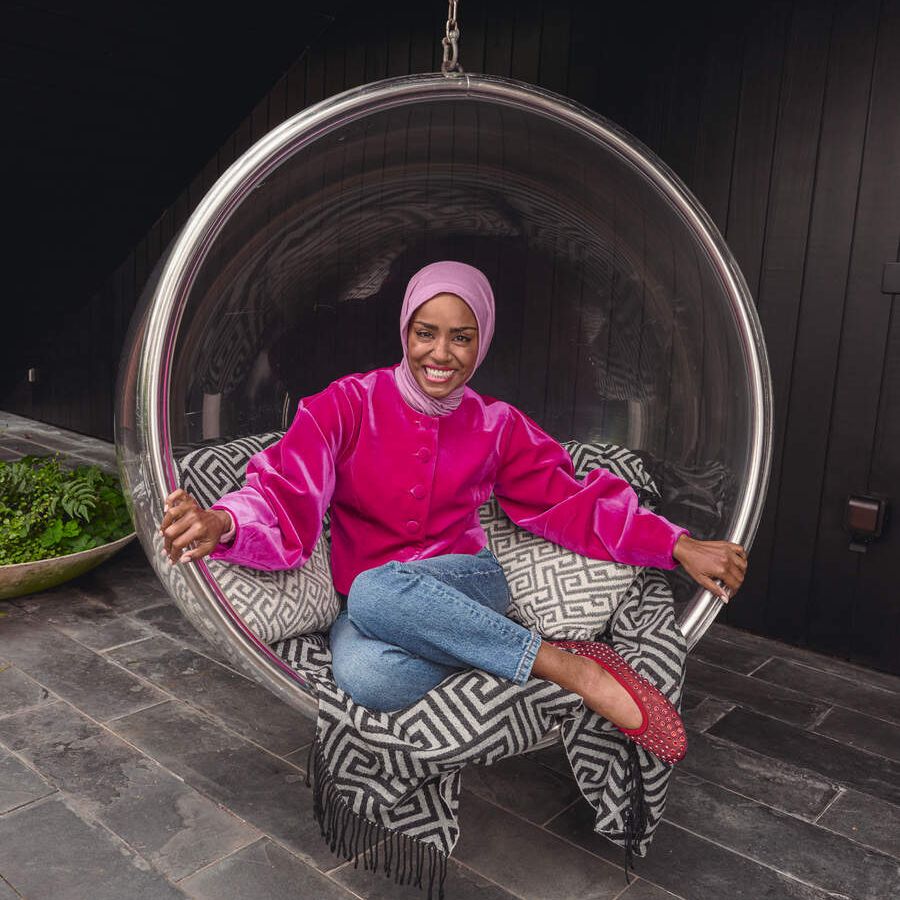 Nadiya Hussain sitting in a floating circe chair with cushions smiling at the camera