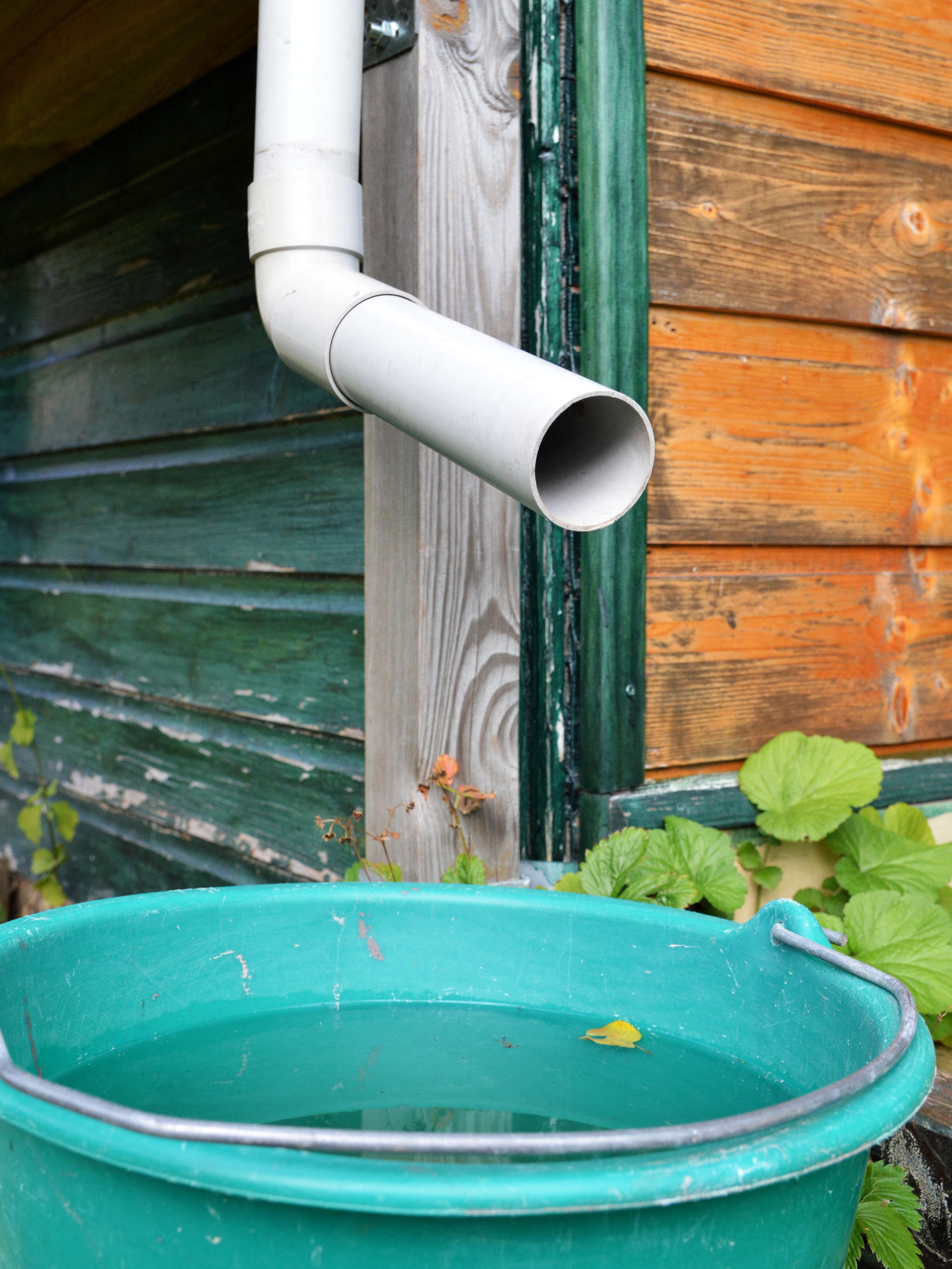 Simple rainwater harvesting setup with downpipe outside stable collecting into a bucket