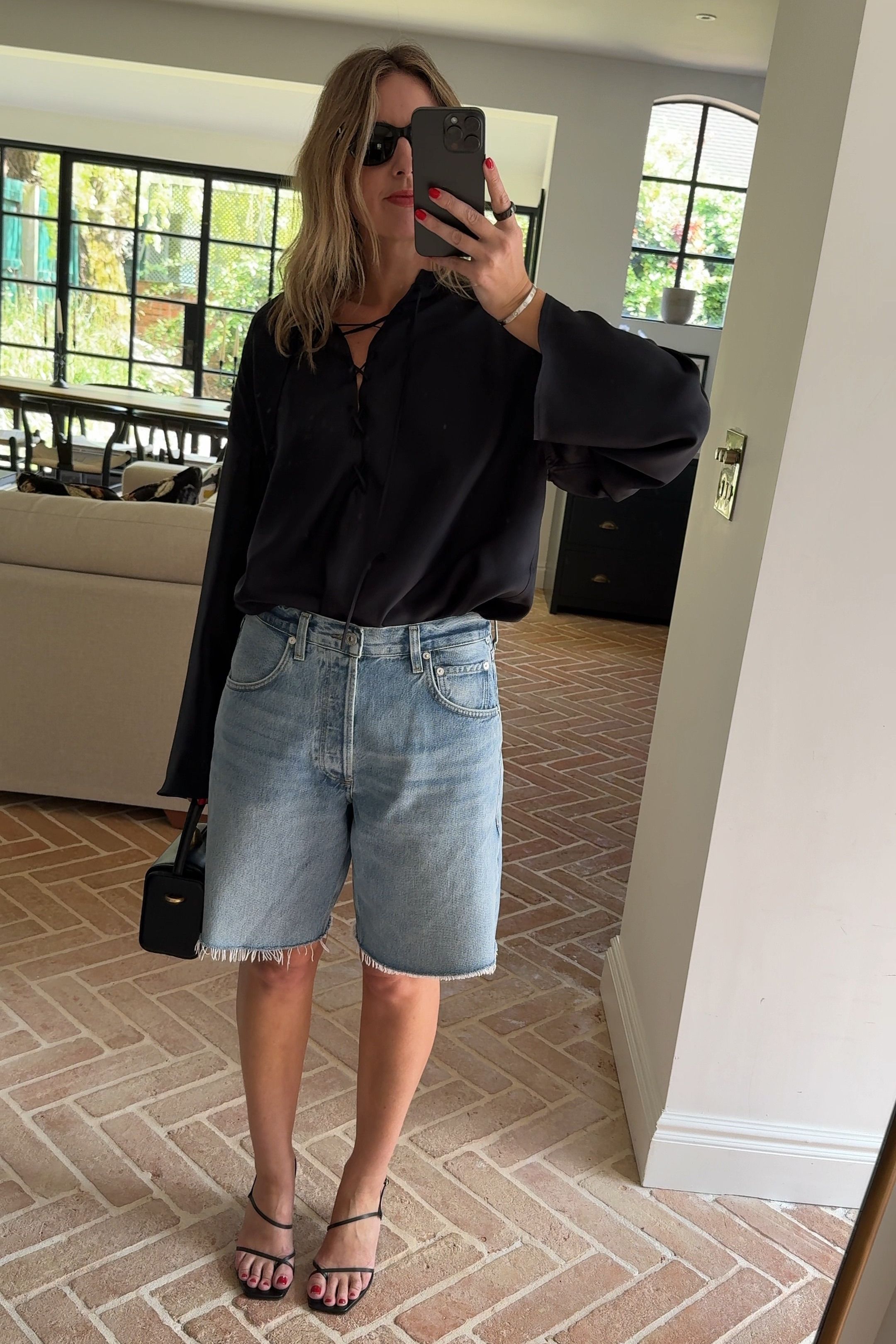 The woman is wearing a black top, blue denim shorts, and black sandals.
