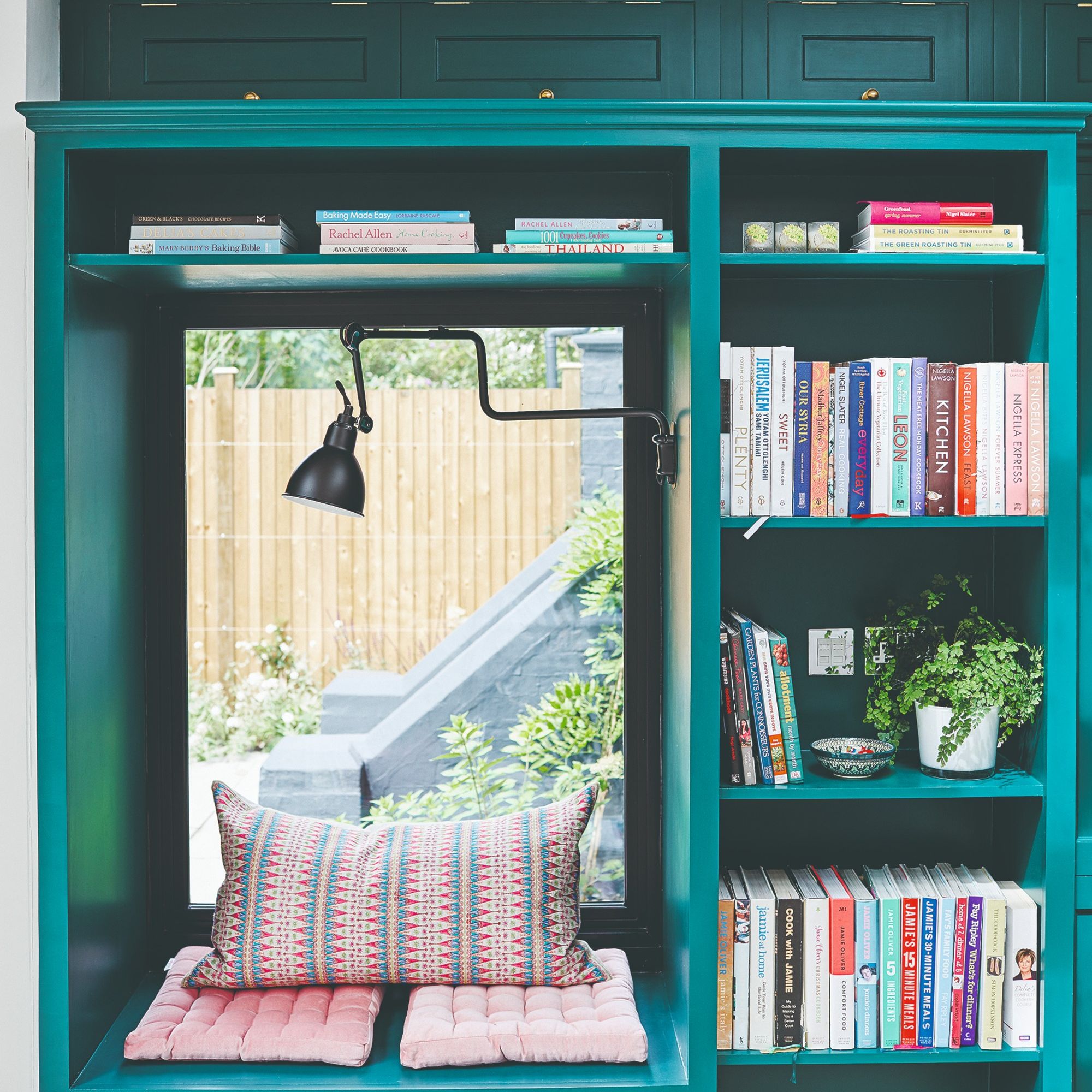 A teal-painted window seat with a built-in bookcase