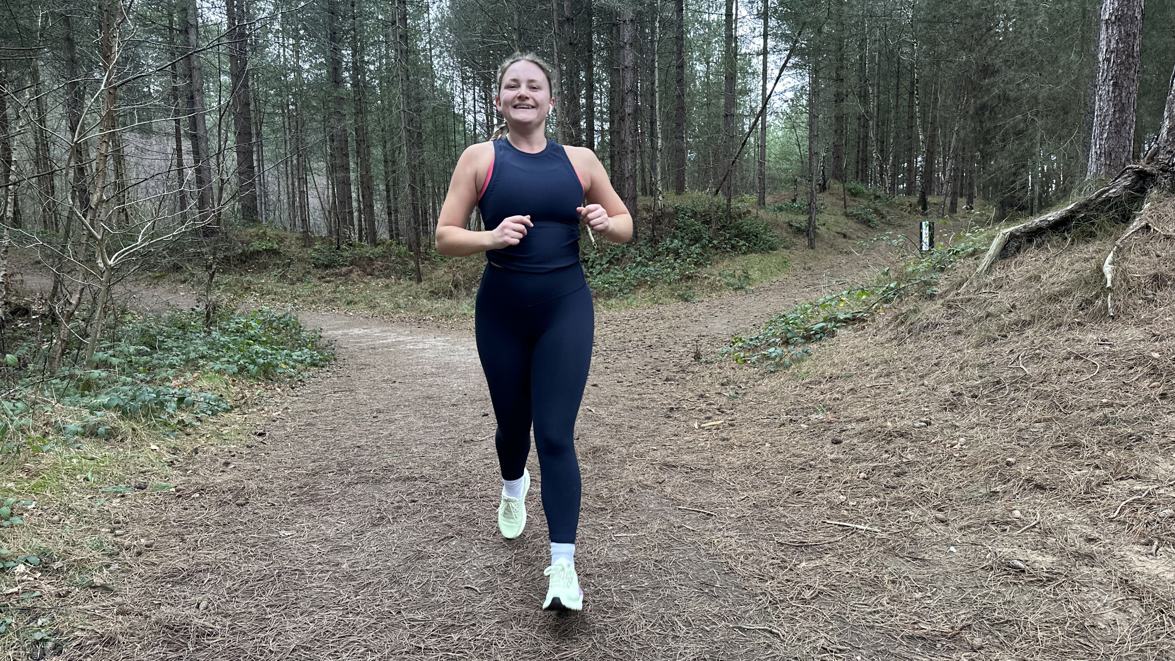 Fitness journalist Alice Porter runs through a forest in leggings and a vest.