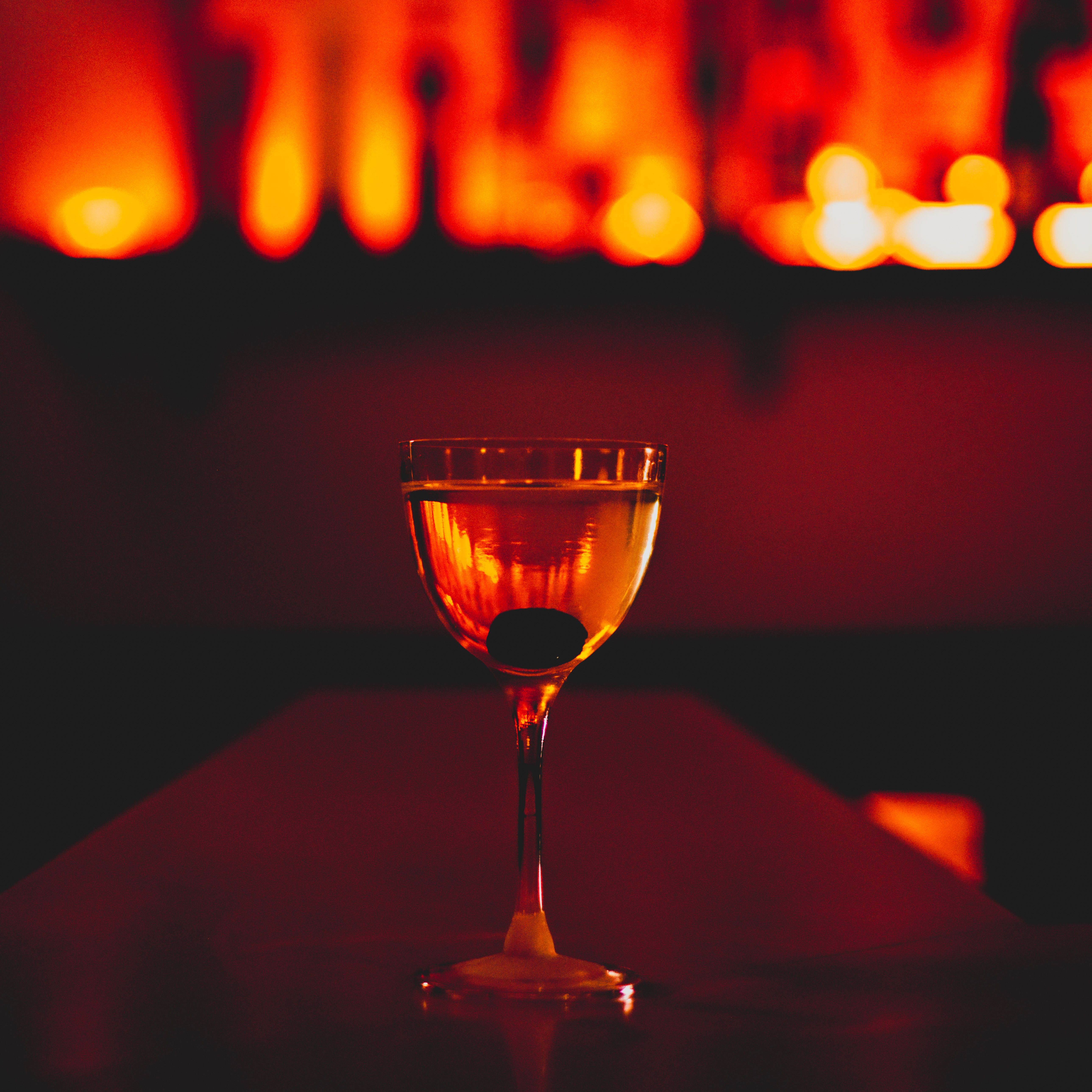 an image of a cocktail in a small martini glass in a low lit red room bar