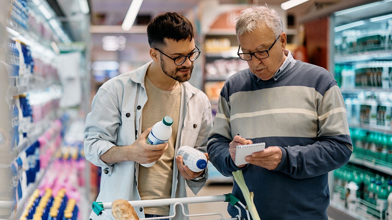 Young man and his senior father going through shopping list while buying in supermarket