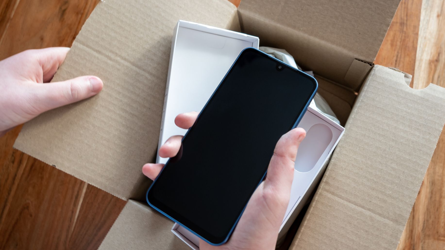 Hand holding new mobile phone after delivery. Unpacking the box with smartphone.