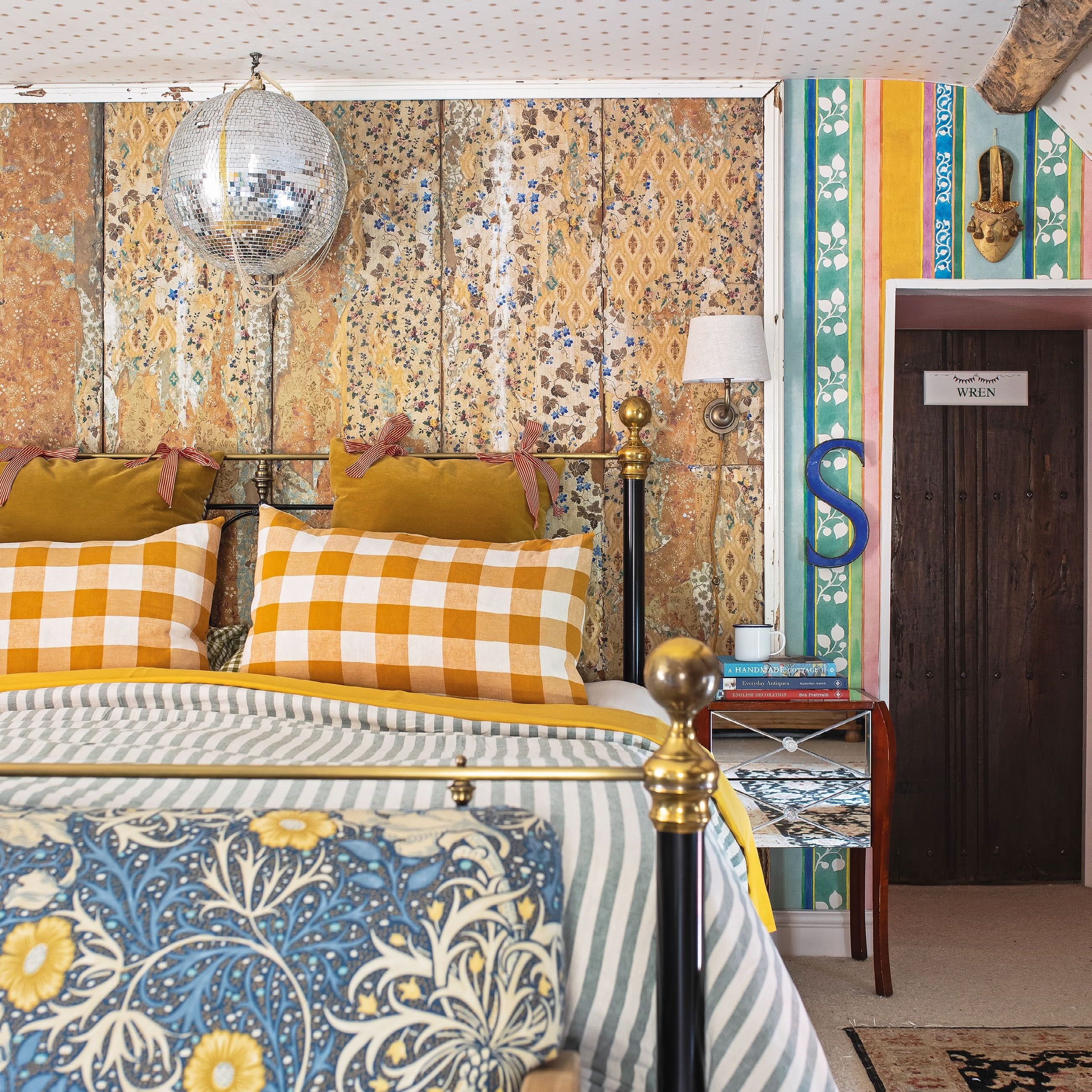 Bedroom with patterned walls and ceiling a mirror ball hanging over bed dressed with stripes and gingham prints