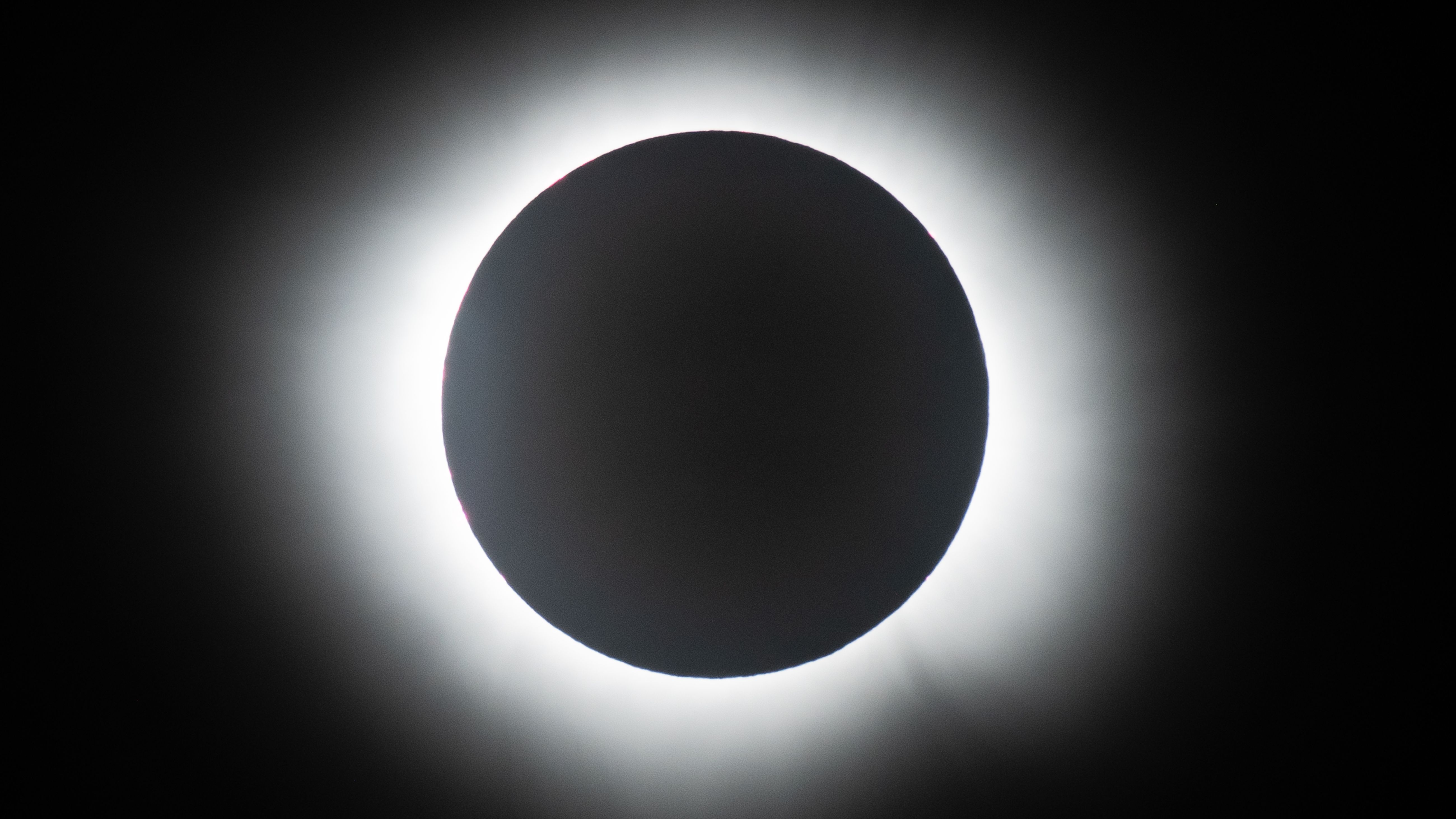 The moon hides the face of the sun in a black sky during a total solar eclipse, allowing its atmosphere to shine around Earth's natural satellite.