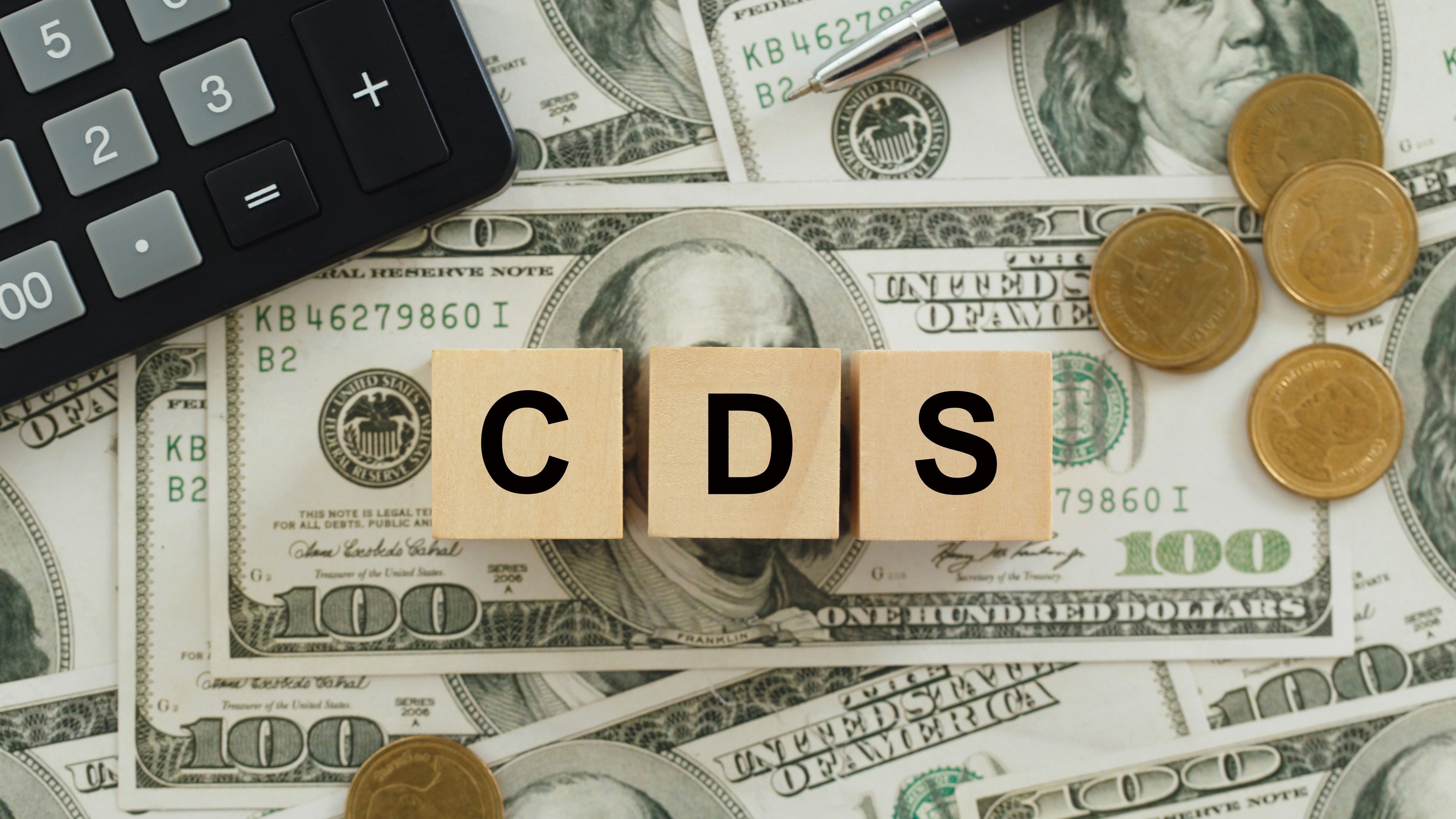Tiles spell out CDS over a background of dollar bills and coins.