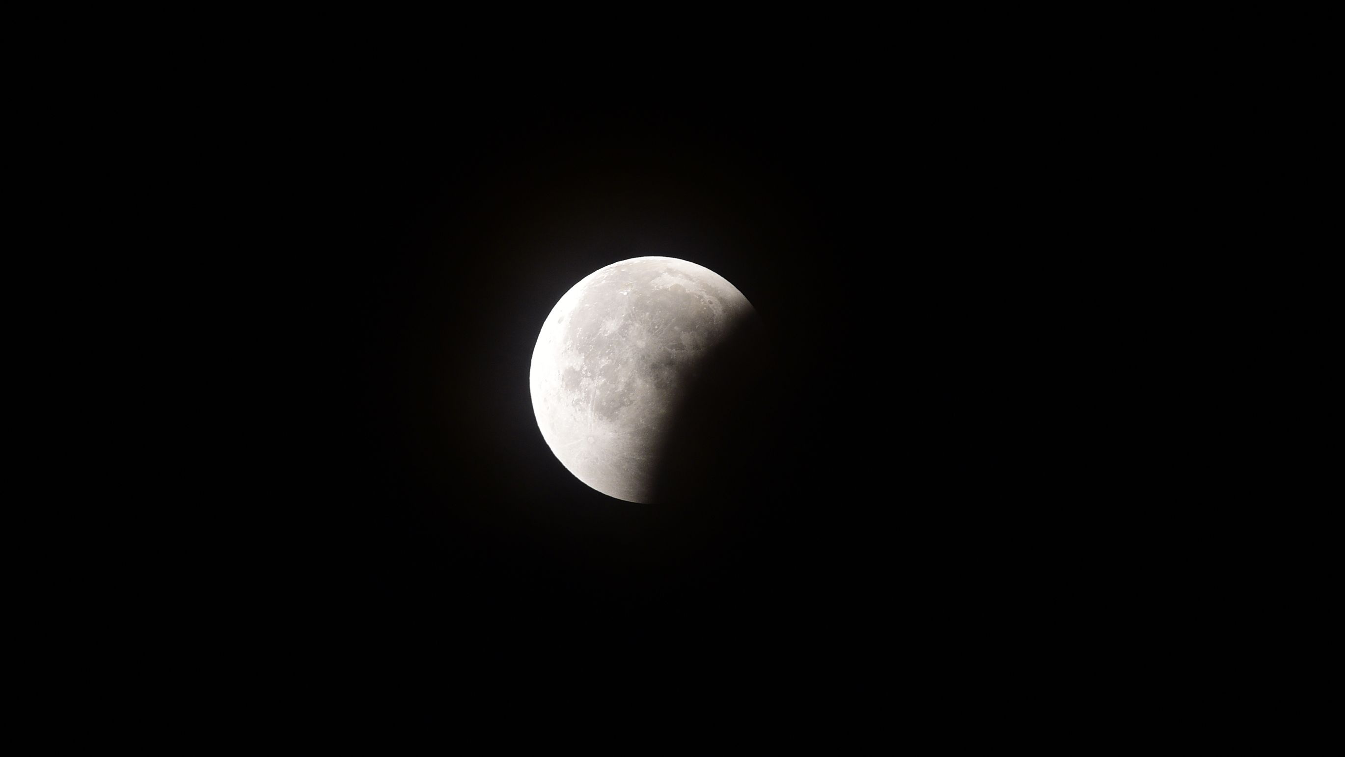 Uma lua cheia é fotografada em um céu negro com sua parte inferior direita escondida pela sombra curva da Terra durante um eclipse lunar.