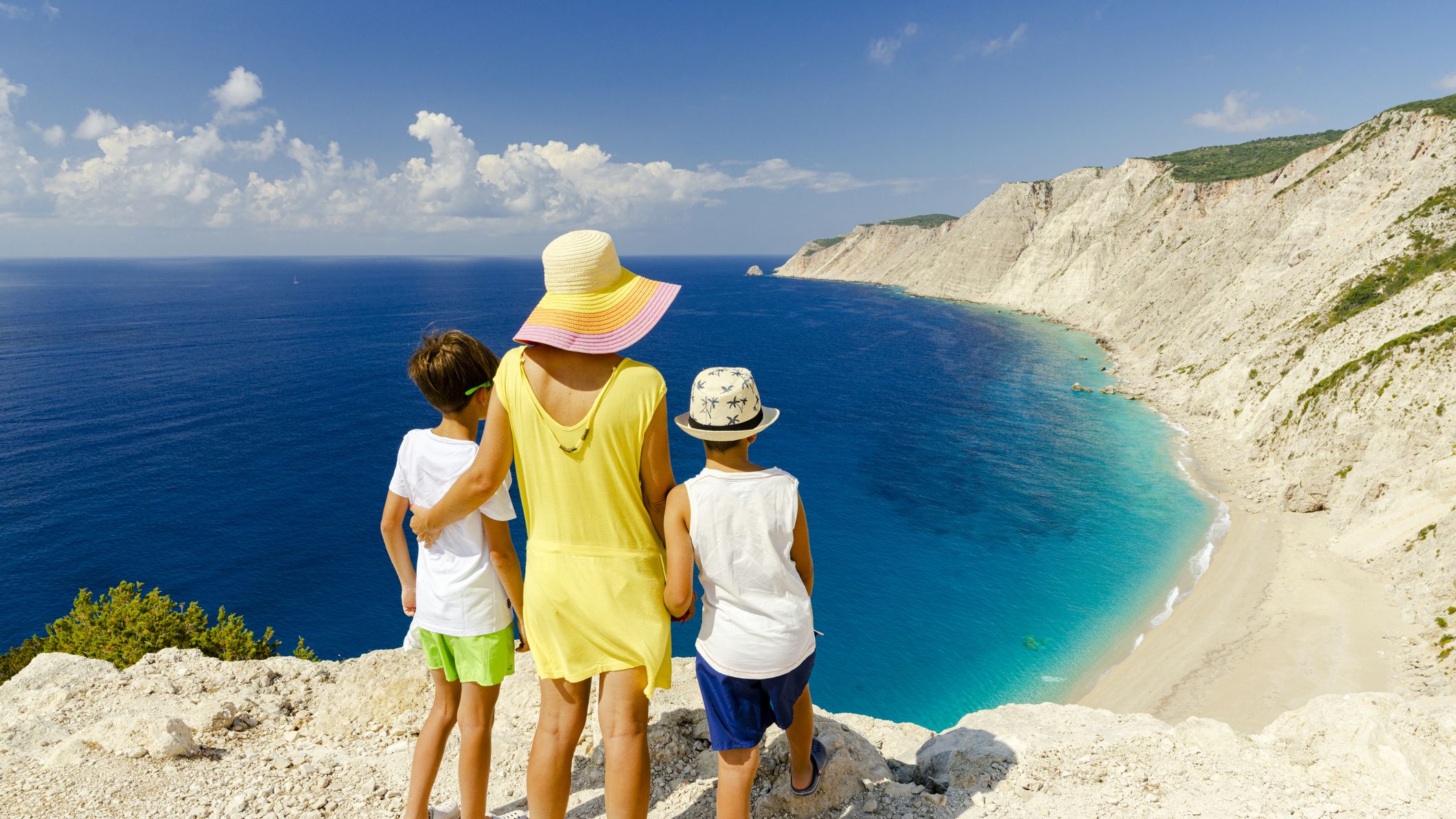 Mother and sons embracing admiring the idyllic Ammos beach standing on top of cliffs, Kefalonia, Ionian Islands, Greece.
