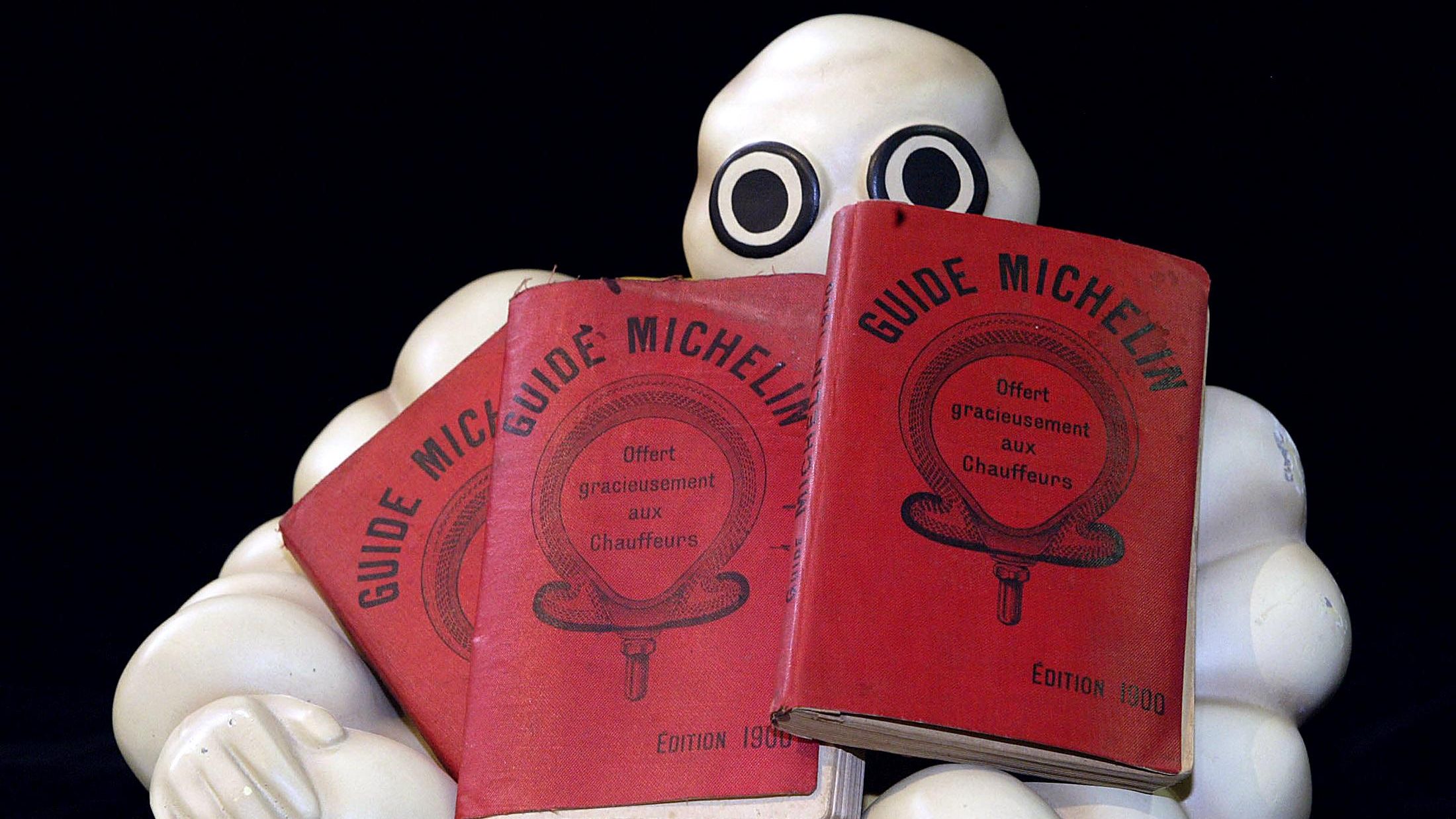an image of three michelin guide booklets from 1900s, being held by a statue of the Michelin man
