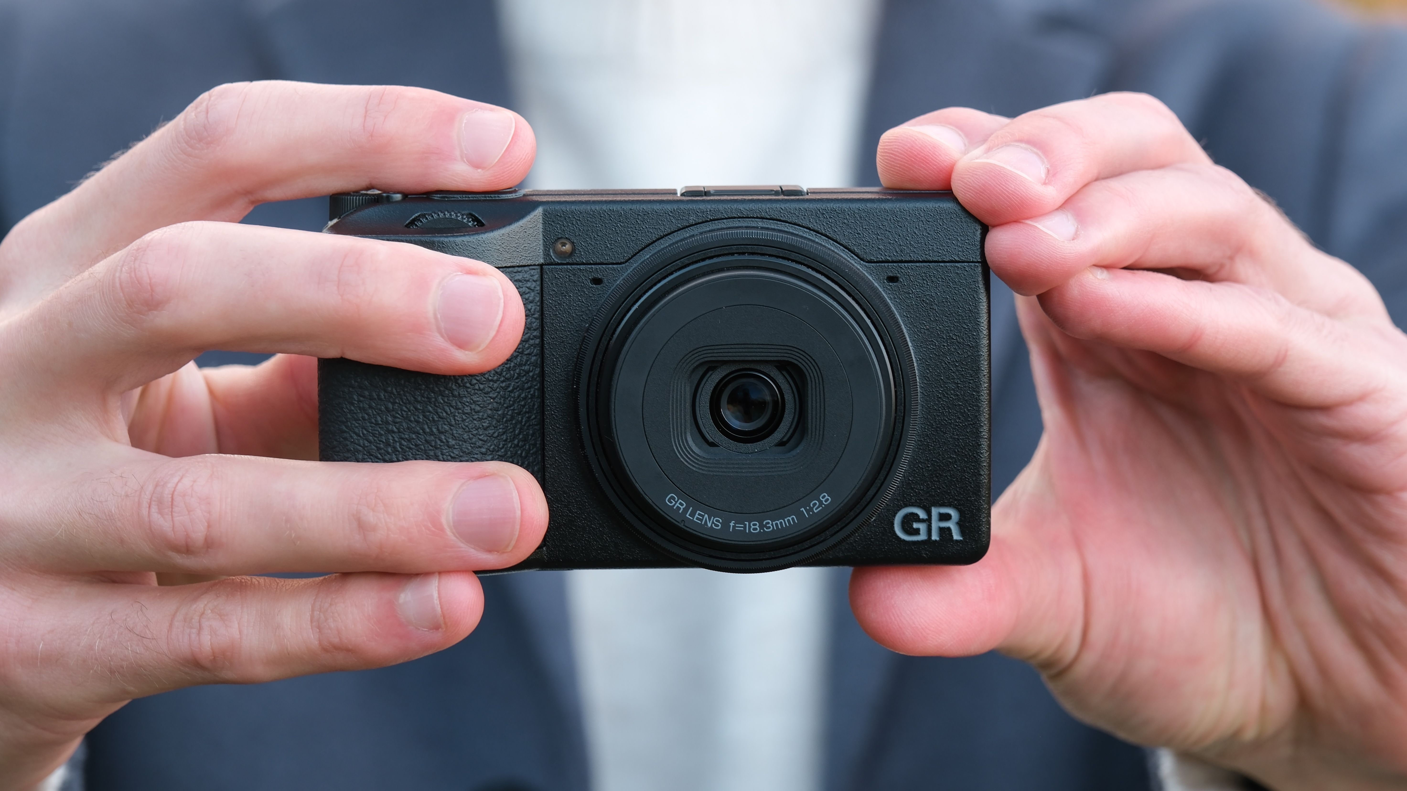 Ricoh GR IV compact camera held in a pair of hands