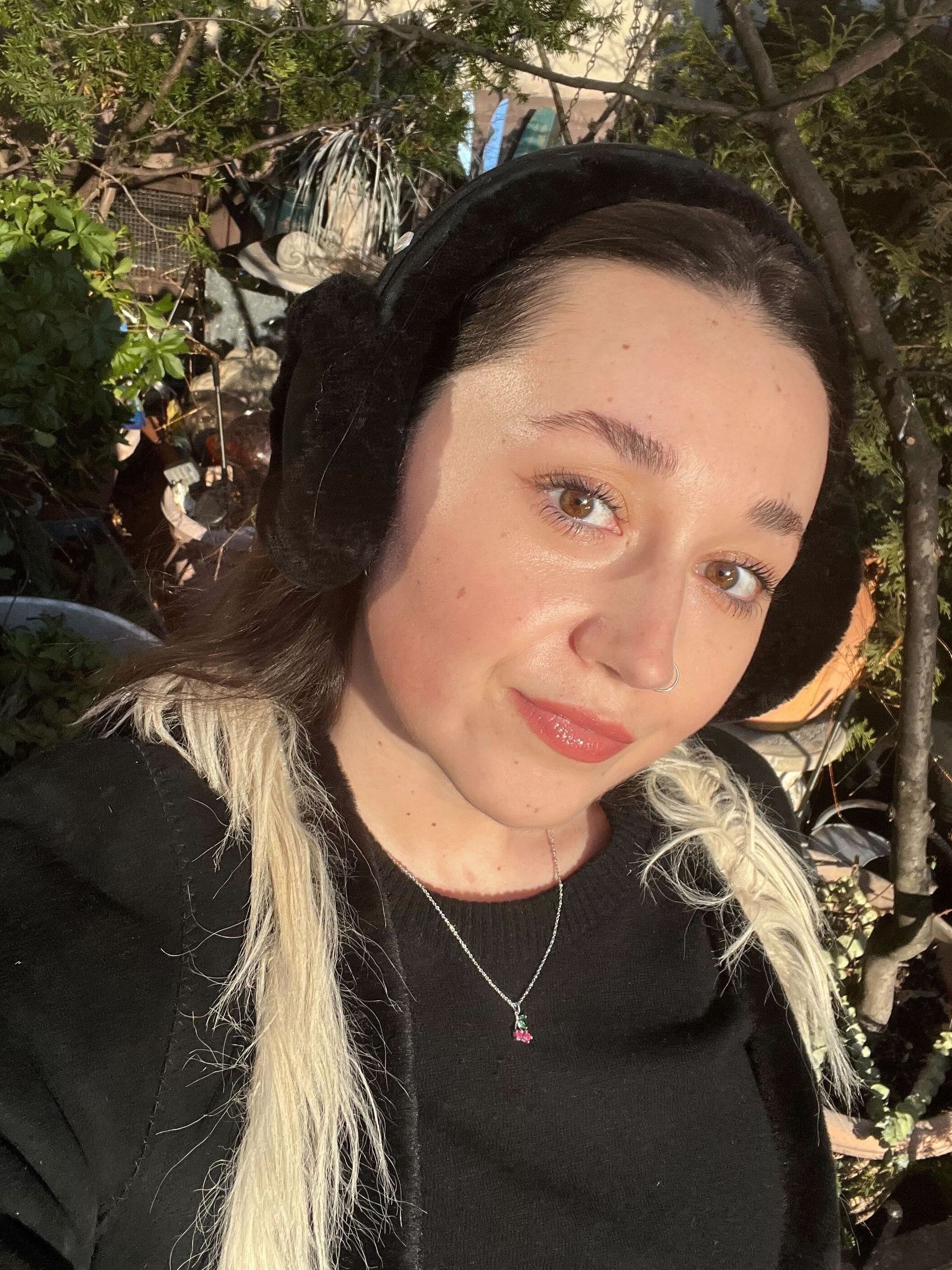 Emma Childs wearing a black sweater, black suede and fur jacket, and black Ugg earmuffs.