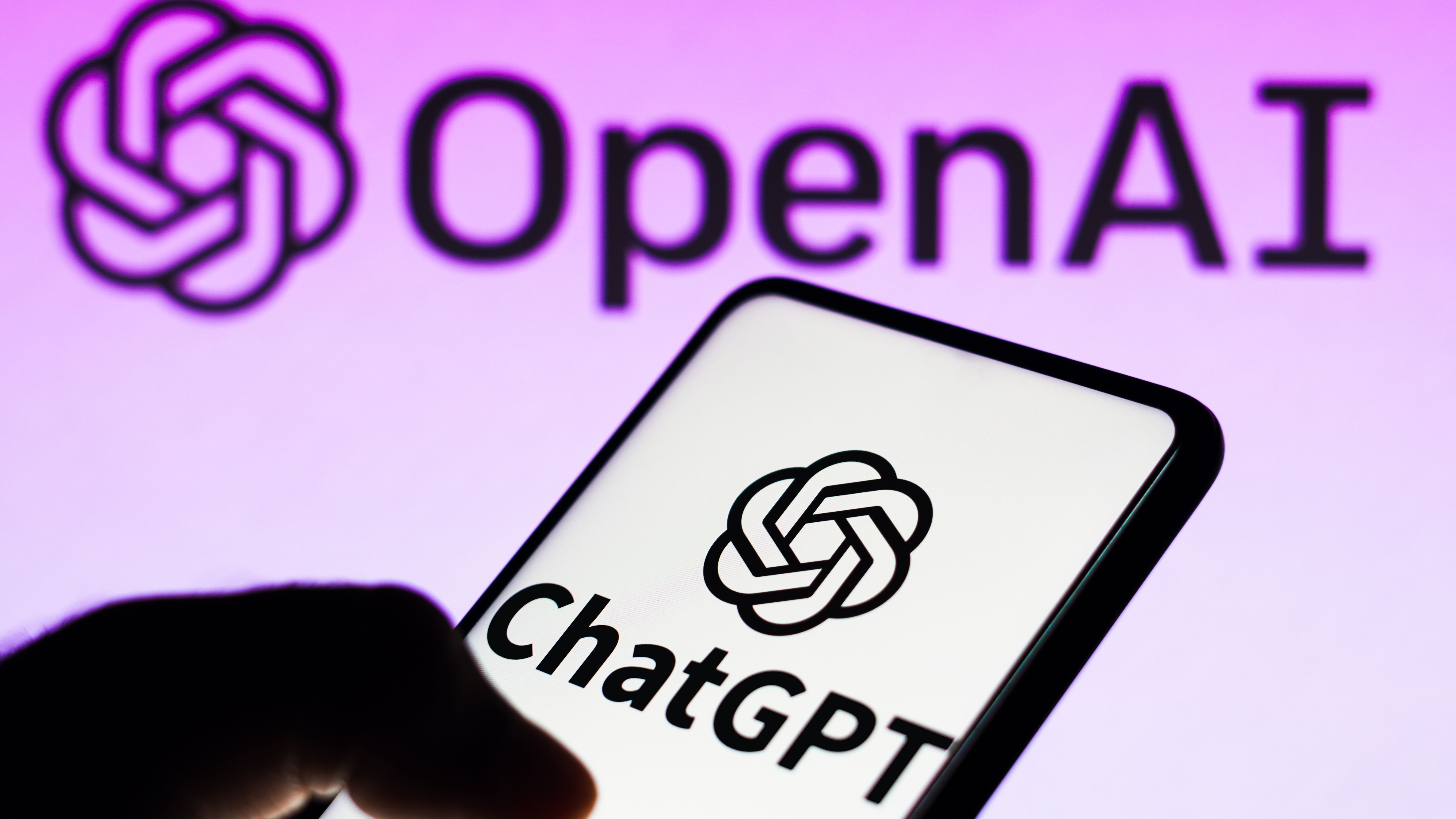 ChatGPT logo on a smartphone with the OpenAI sign in the background