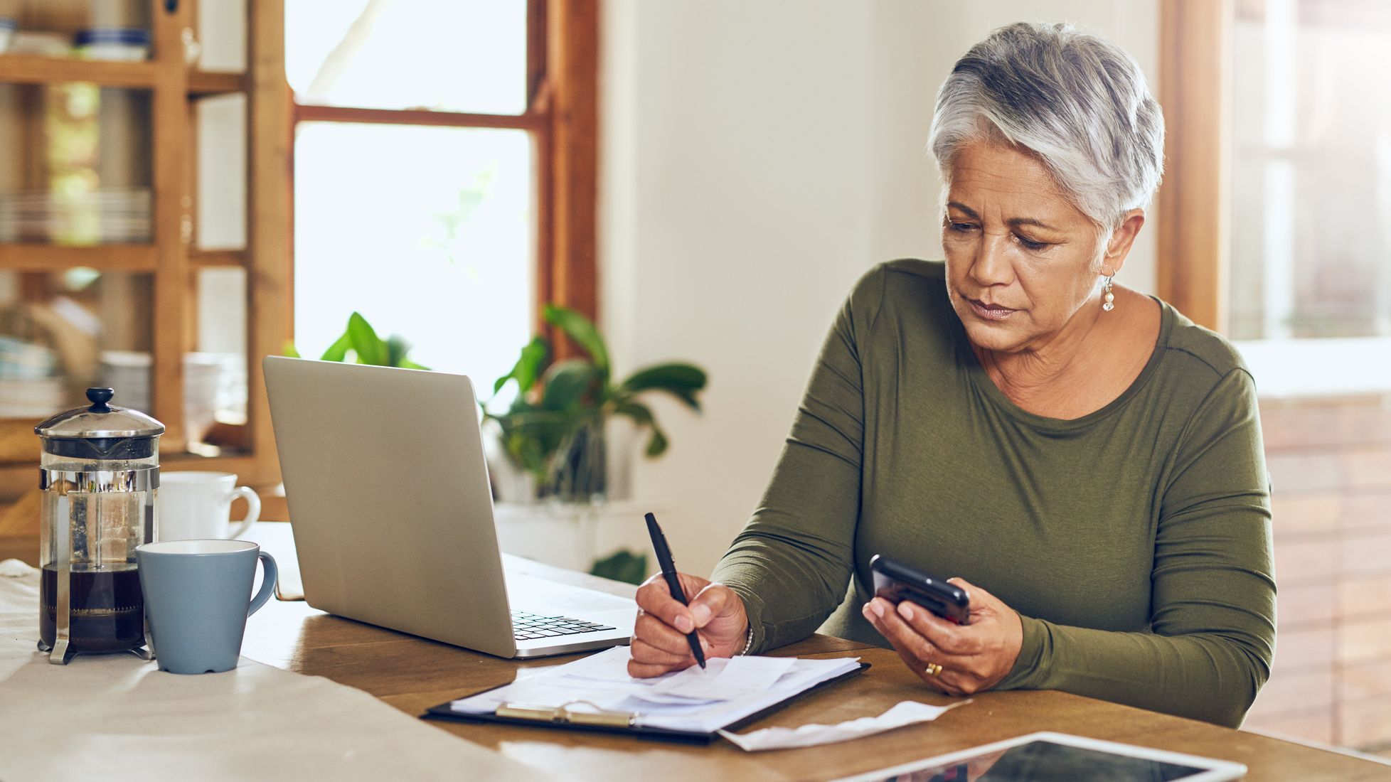 A middle-aged woman reviewing her finances at her dining table.
