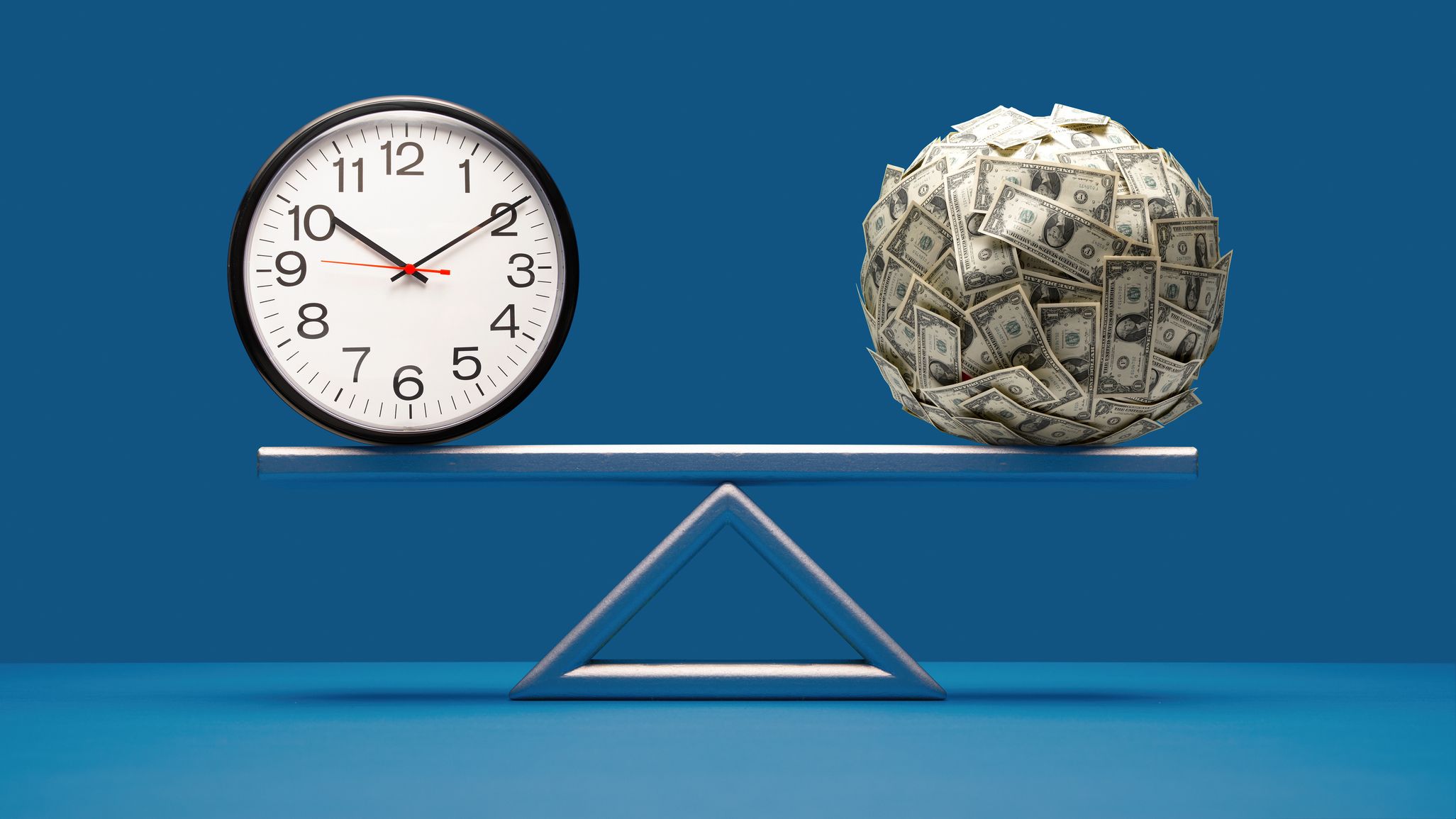 analog clock and ball of US paper currency equally balanced on seesaw weight scale on blue surface and background