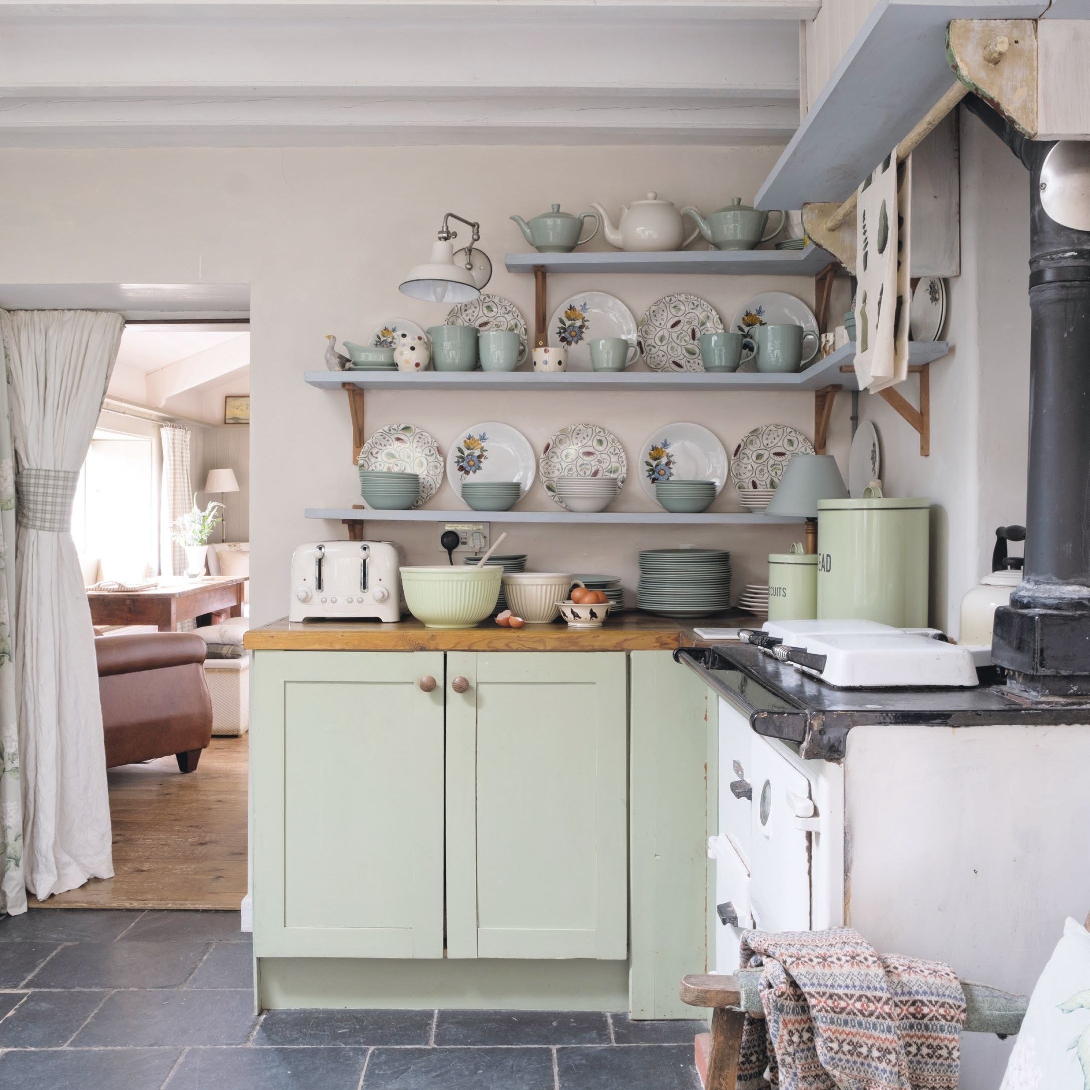 Corner of a country cottage kitchen with white range cooker, green kitchen cupboards and blue painted open shelves