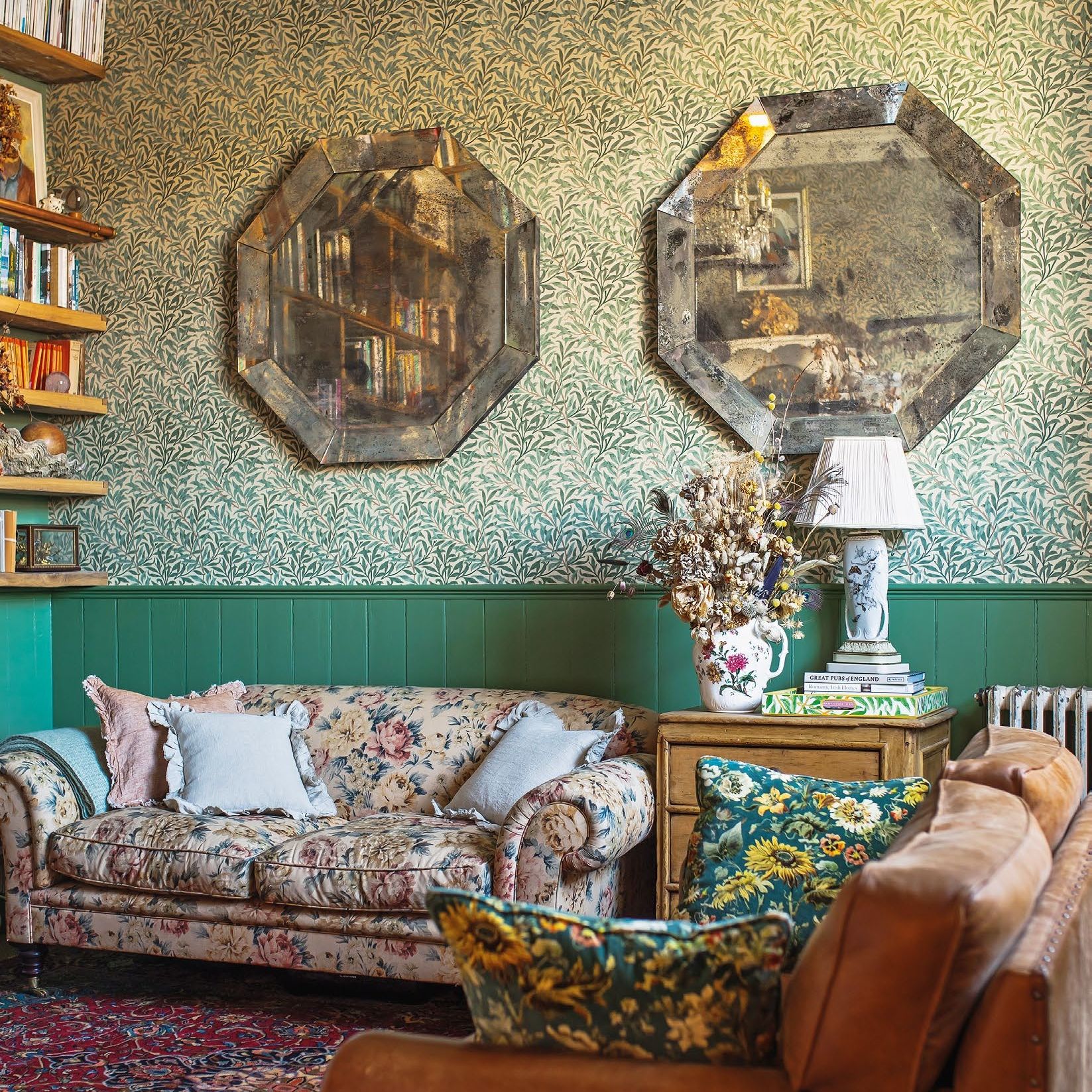 Cottage living room with green patterned wallpaper, floral sofa, oriental rug and two octagonal mirrors on wall