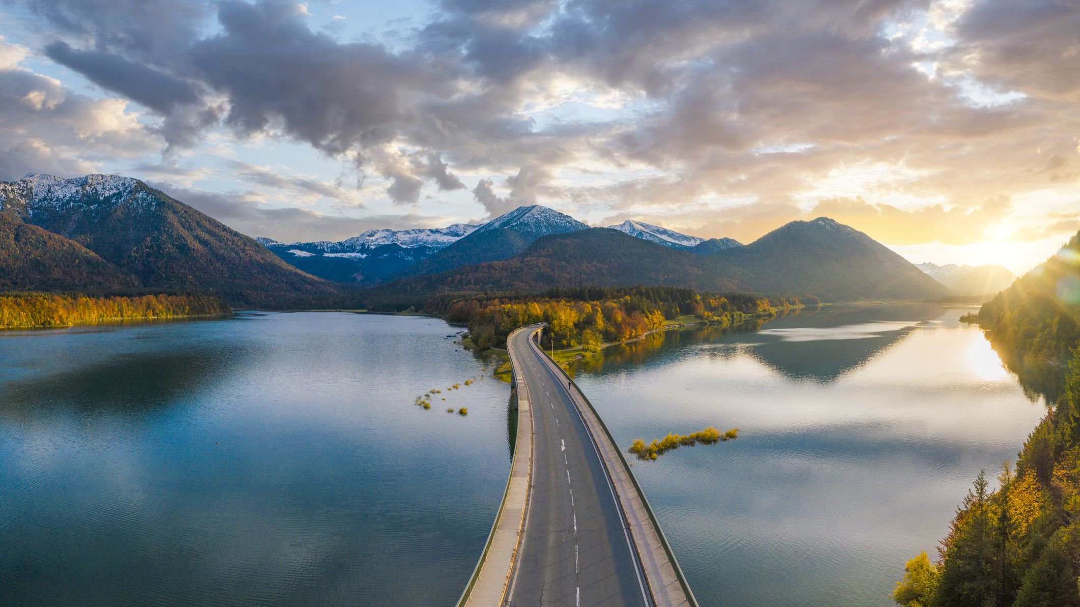 An idyllic bridge over Sylvenstein Lake, Germany. It is sunrise or sunset and the bridge goes over the lake to mountains.