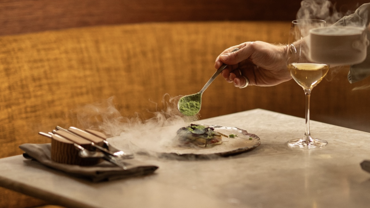 an image of a dish being plated on a table, with smoke and steam around it
